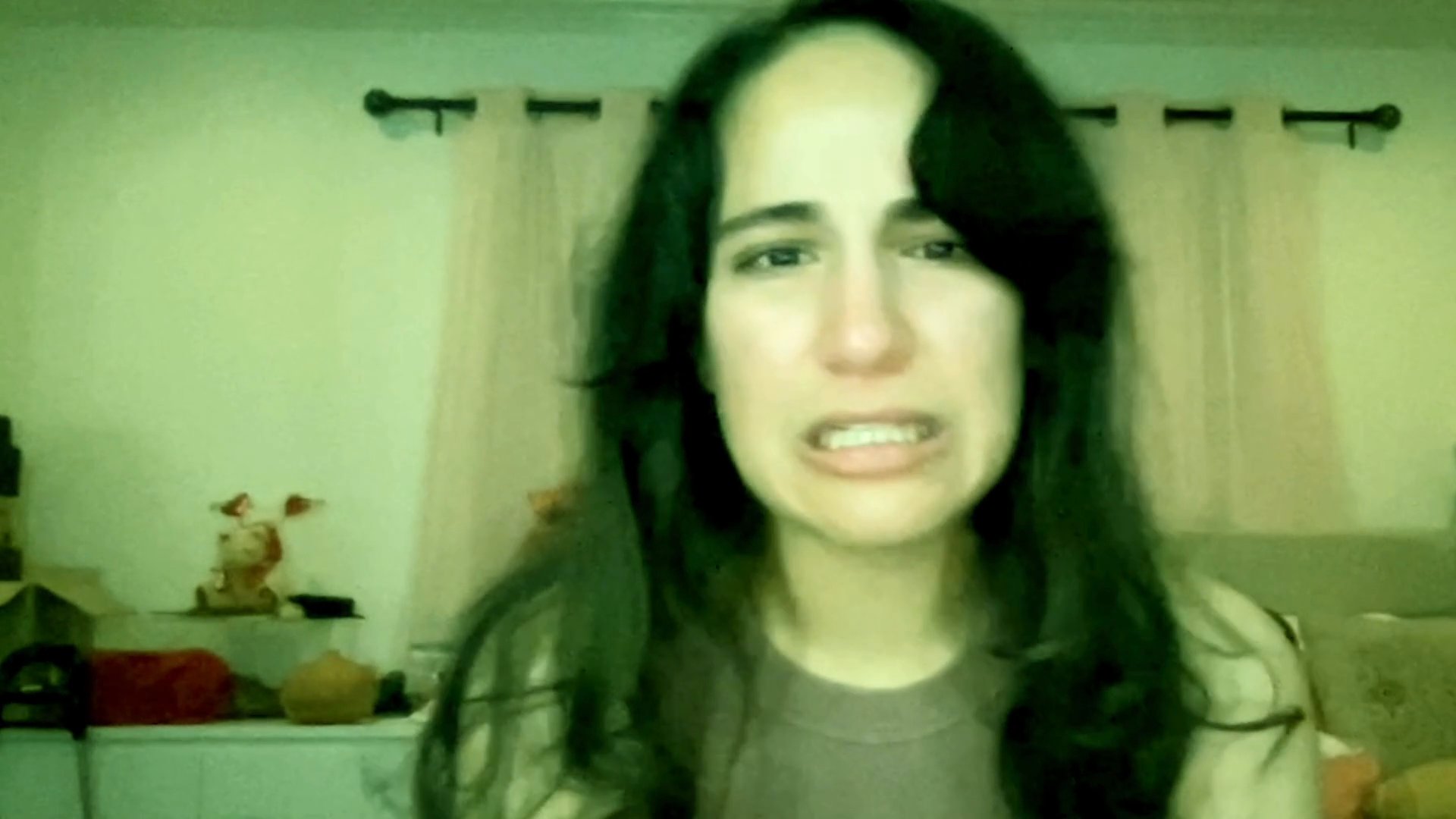 A woman sits in a room while visibly experiencing significant emotional distress and crying. Her facial expressions and demeanor convey a state of deep personal upset.