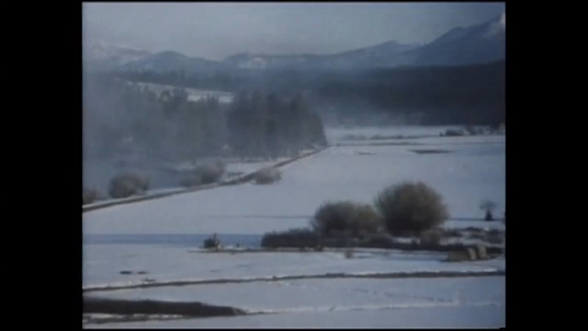 A woman in a brimmed hat looks pensively downward before a wide view reveals snow-covered fields and distant hills at Pine Ridge Ranch in Oregon. Piano music accompanies her words about the roar and rattle of cattle.