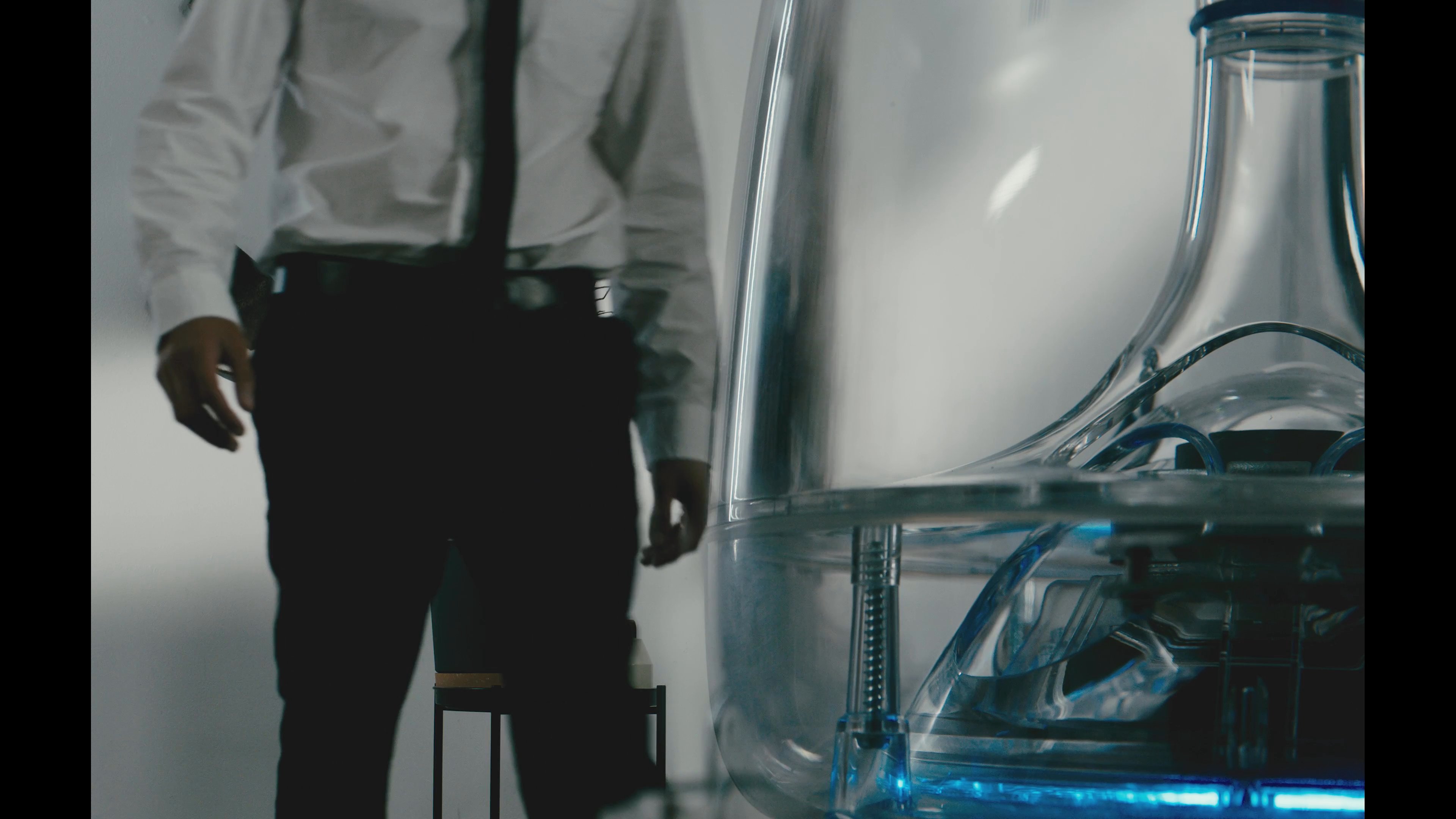 A man places a modern, transparent humidifier on a coffee table in a contemporary living room. The device emits a gentle, glowing mist to improve the interior atmosphere.
