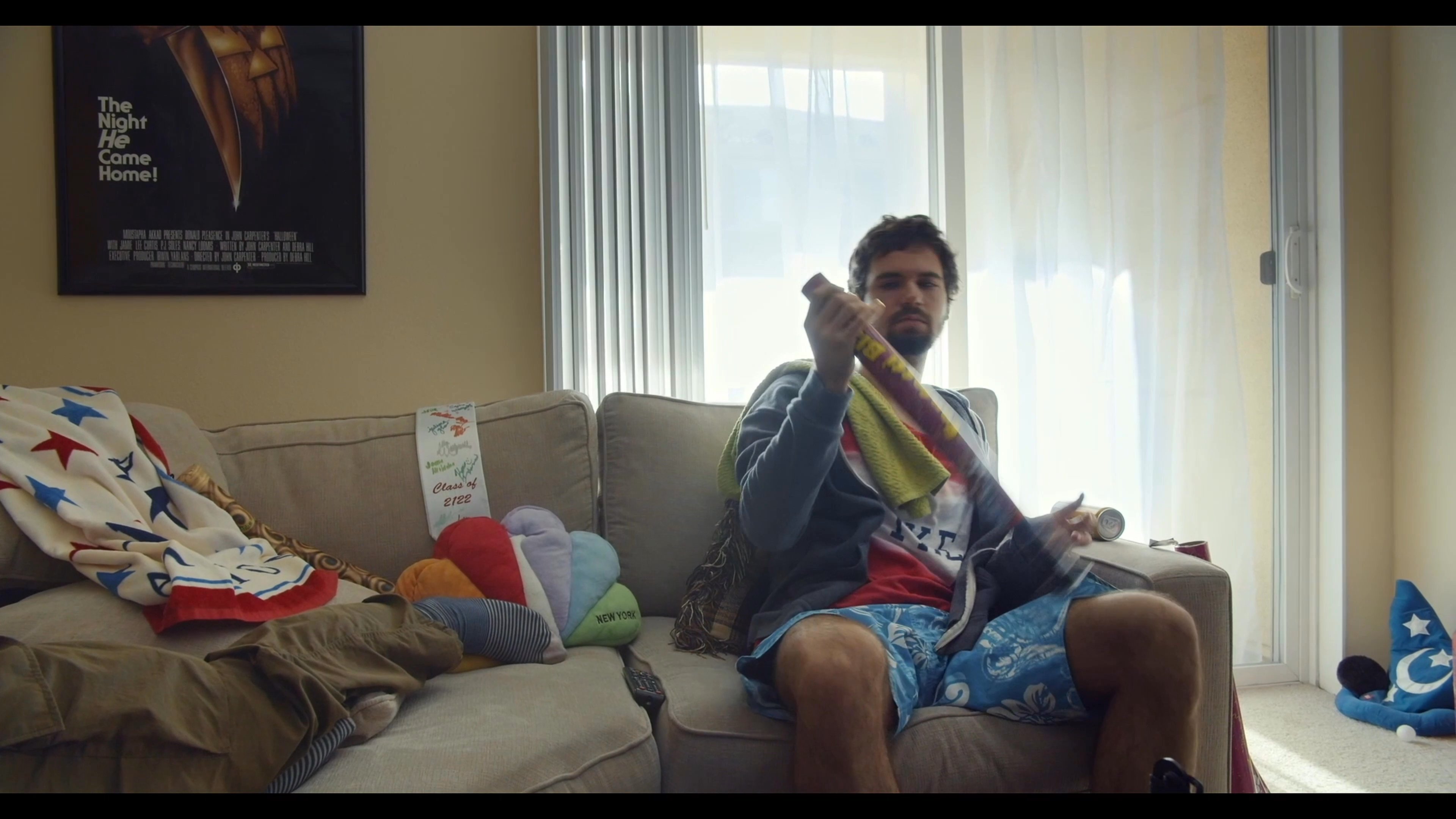 A man experiences a moment of solitary celebration in his living room by firing a handheld confetti cannon. After the initial burst, he sits amidst the scattered paper, reflecting on the quiet scene.