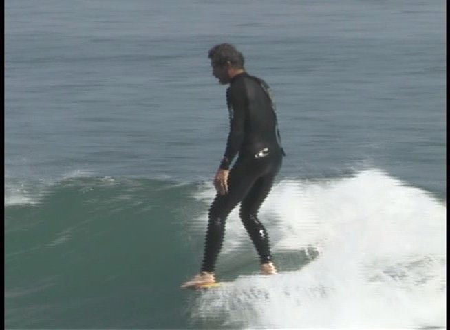 A surfer wearing a wetsuit skillfully rides an ocean wave, maintaining balance and posture while maneuvering across the surface of the water.
