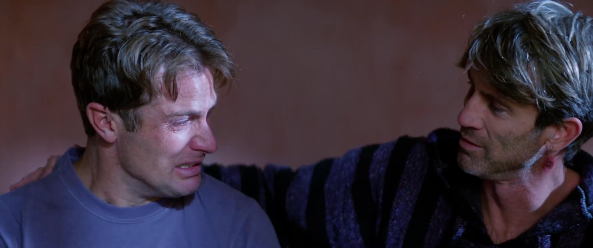 One man offers emotional solace and physical reassurance to his grieving companion who is weeping. This intimate interaction emphasizes themes of empathy and shared human vulnerability.