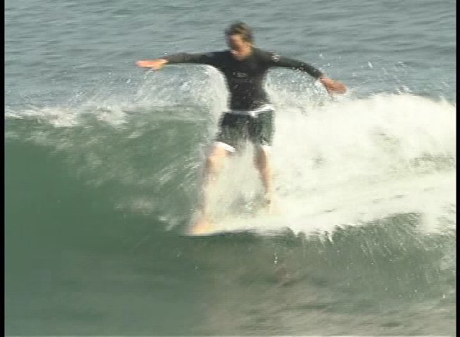 A skilled longboarder glides across ocean waves, maintaining balance and maneuvering through the surf.