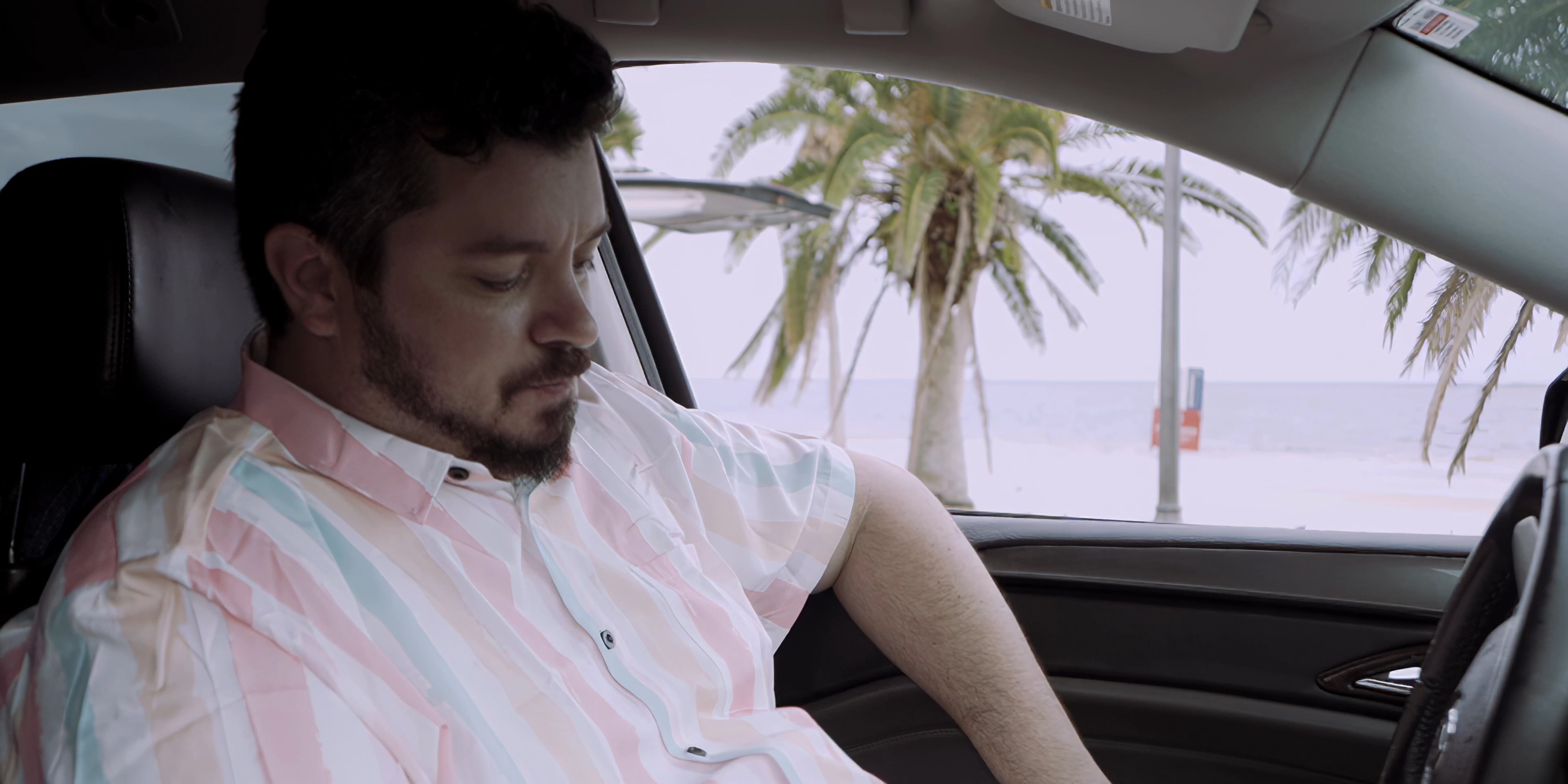 A man sits in his parked vehicle while engaged in a video conversation with his son, who appears on a mounted smartphone screen. They exchange dialogue while maintaining visual contact through the mobile interface.