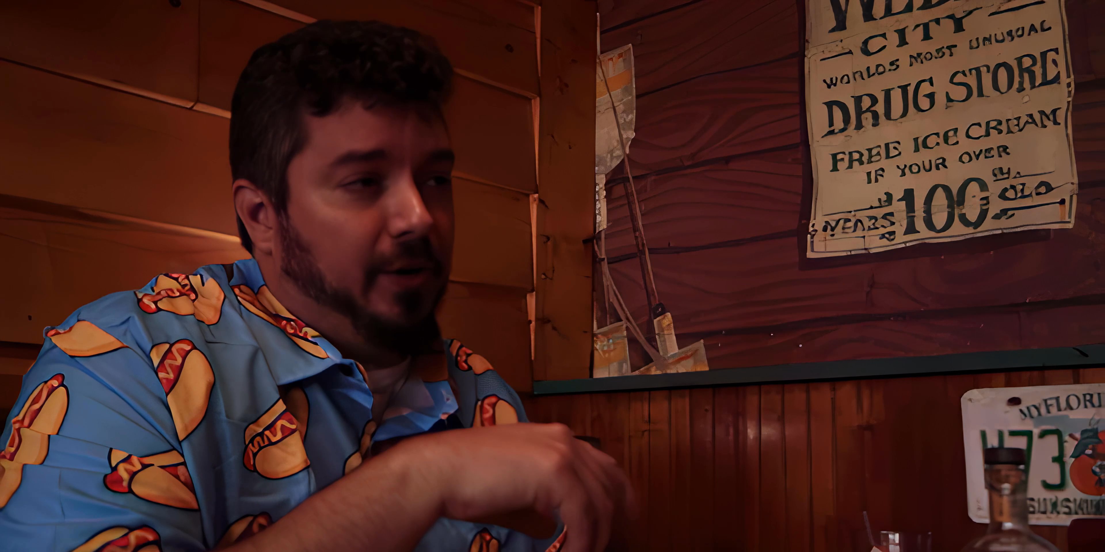Two men engage in a serious, focused conversation while sitting at a wooden table in a retro-style diner booth. The interaction transitions from a two-person exchange to a focused close-up on one individual as he gestures and speaks.