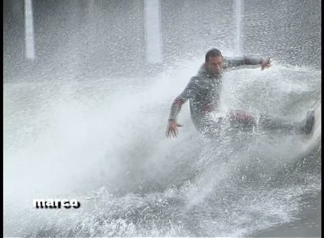 Surfers maneuver across dynamic waves near a wooden pier structure. The participants exhibit advanced board control while navigating the turbulent coastal environment.