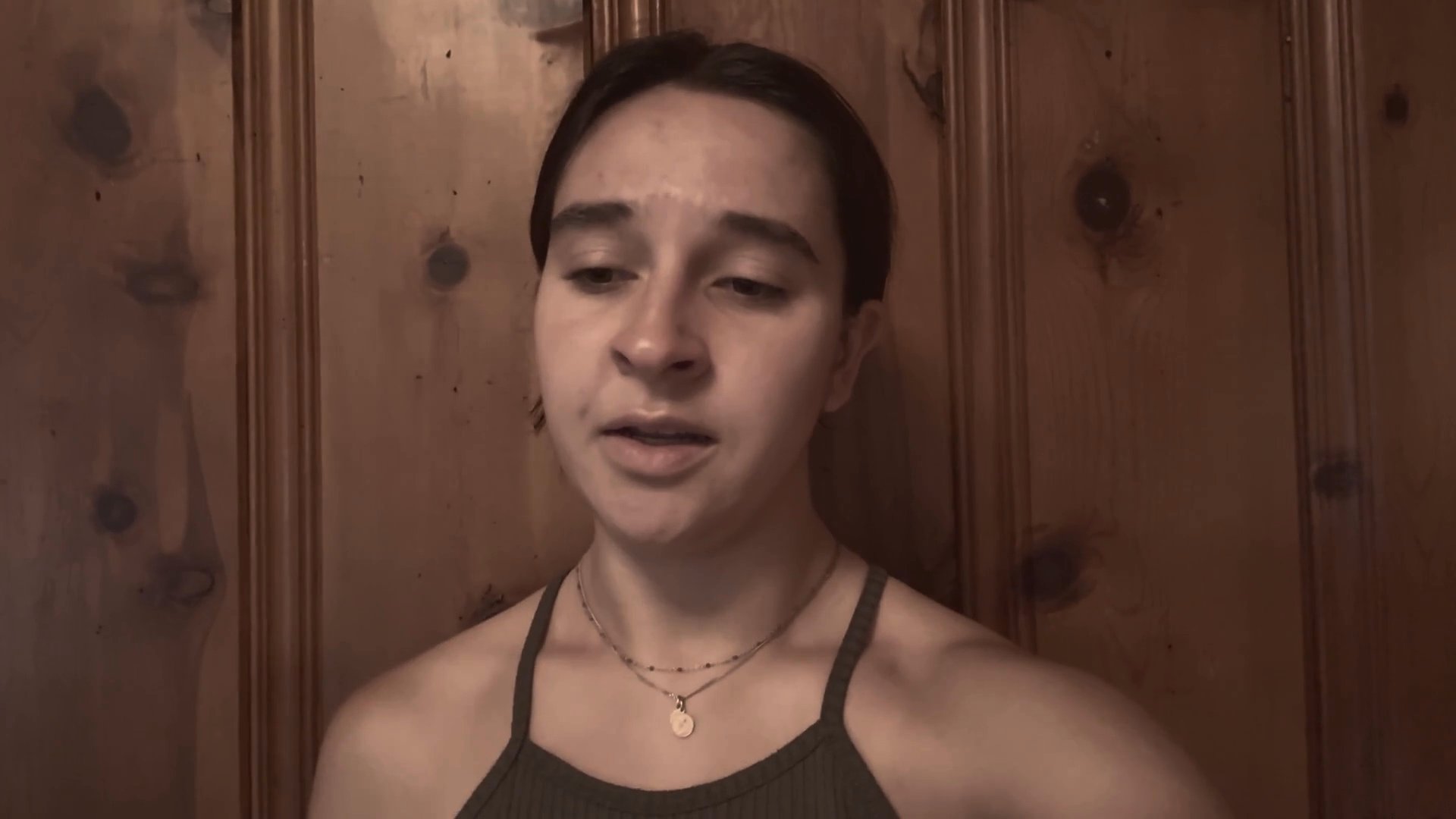 A young woman delivers an emotional and expressive monologue while positioned against a wooden-paneled wall. She maintains direct eye contact with the camera, utilizing facial expressions to convey a narrative.