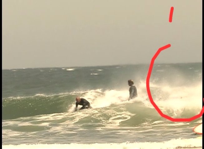 Surfers engage with the ocean waves while wearing wetsuits, with a large naval vessel visible in the background. The sequence captures various attempts at wave riding and maneuvering within the surf.