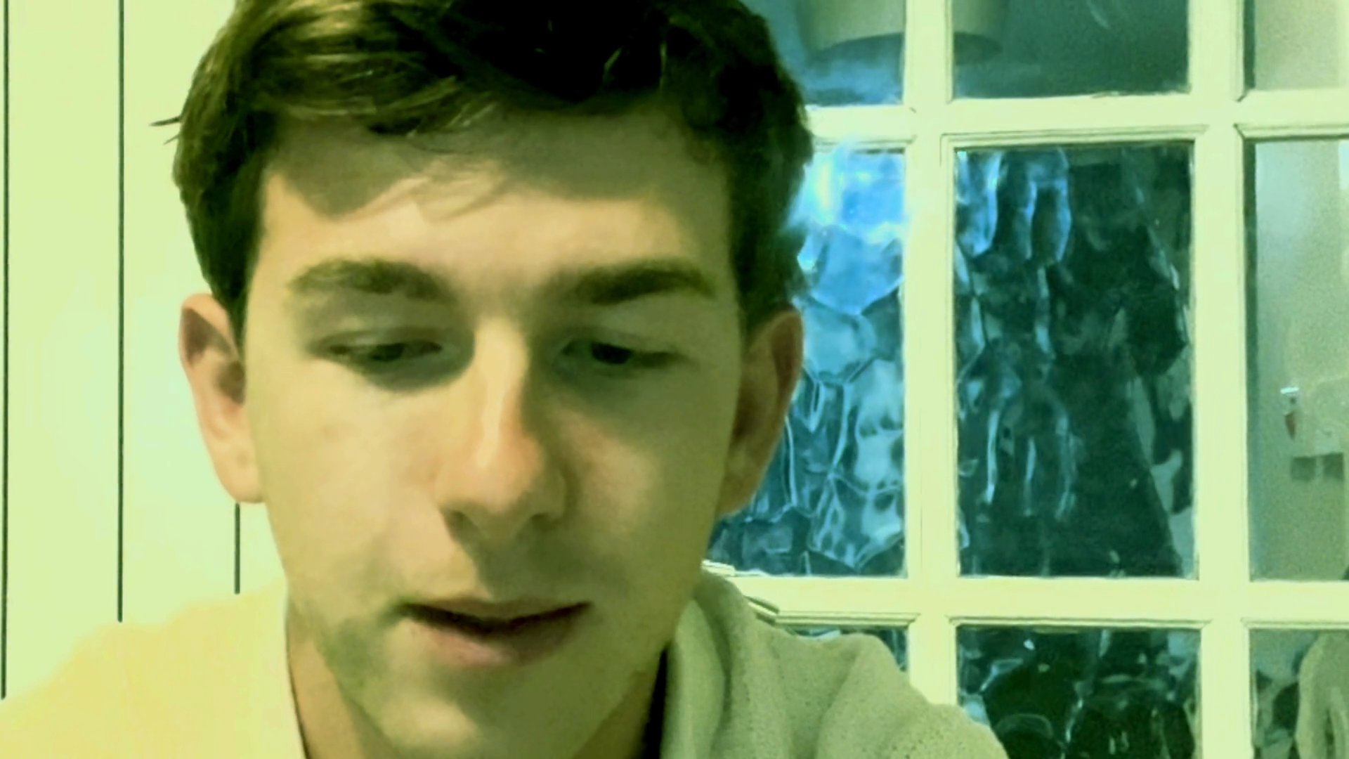 A young man sits indoors and speaks directly to the camera, delivering a focused monologue or personal commentary.