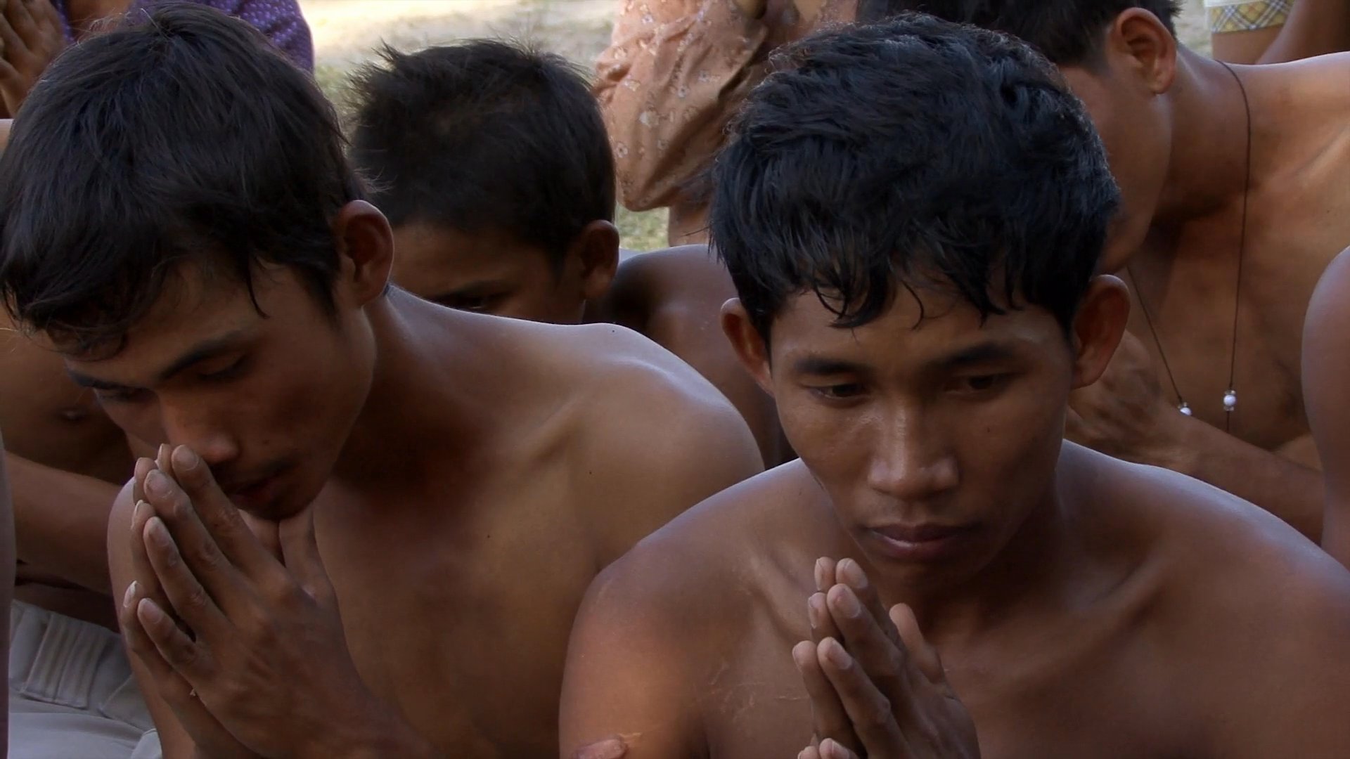 Monks and community members participate in a formal prayer gathering in an outdoor, rural setting. Participants engage in shared meditative reflection while receiving guidance from spiritual leaders.