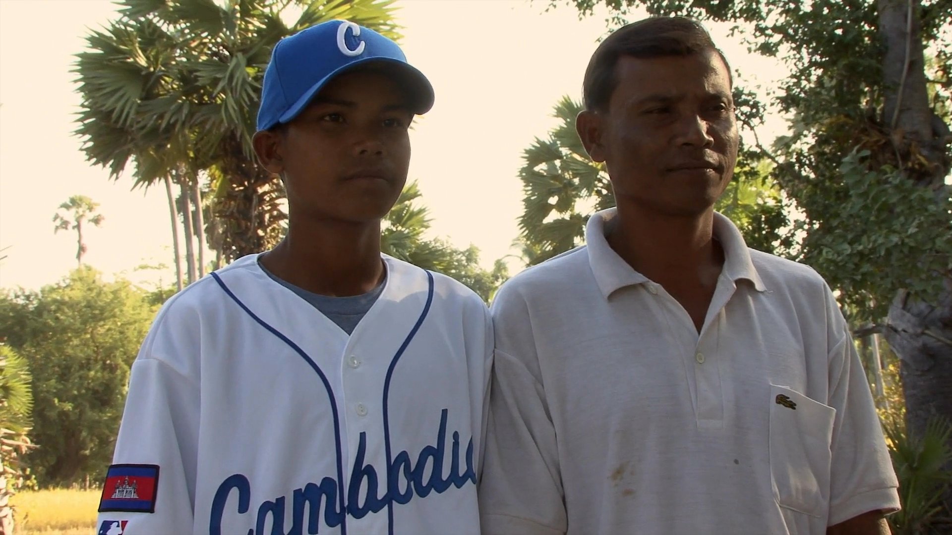Young baseball players in Cambodia meet with family members on a field before training together as a team.