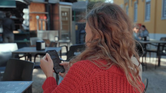 A girl sitting at an outdoor café using her smartphone and eating ice cream