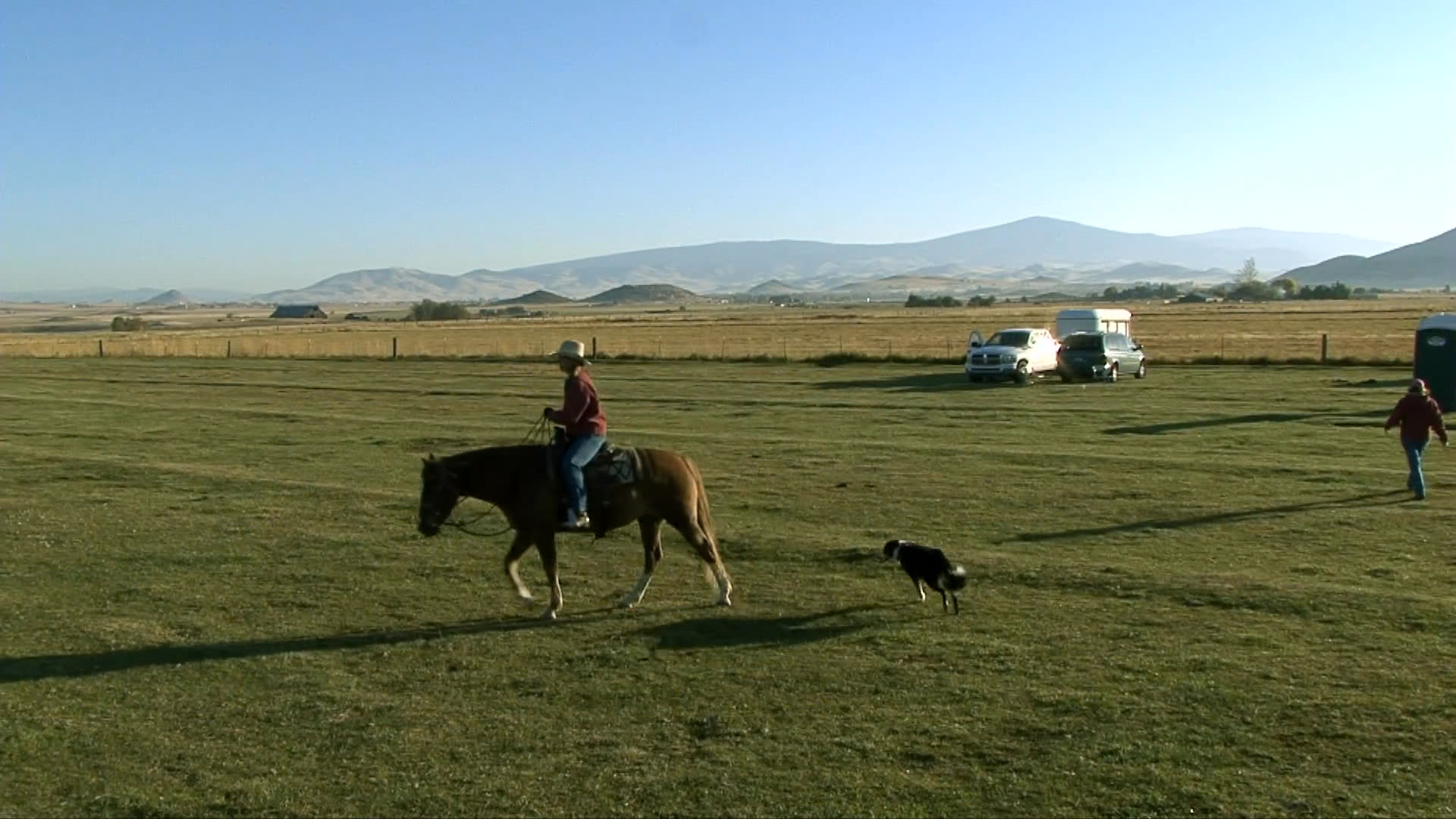 A man interacts with dogs on a coastal beach before transitioning to a scenic sequence of a person horseback riding through a grassy field in Yreka, California.