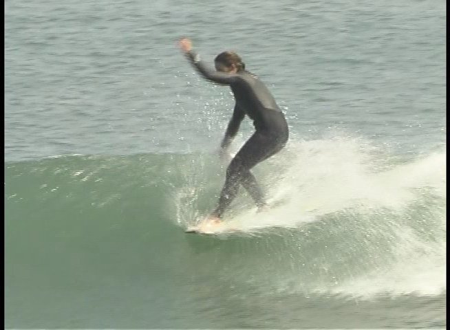 A surfer demonstrates riding a wave in the ocean, followed by an expert providing commentary and analysis in an outdoor setting.
