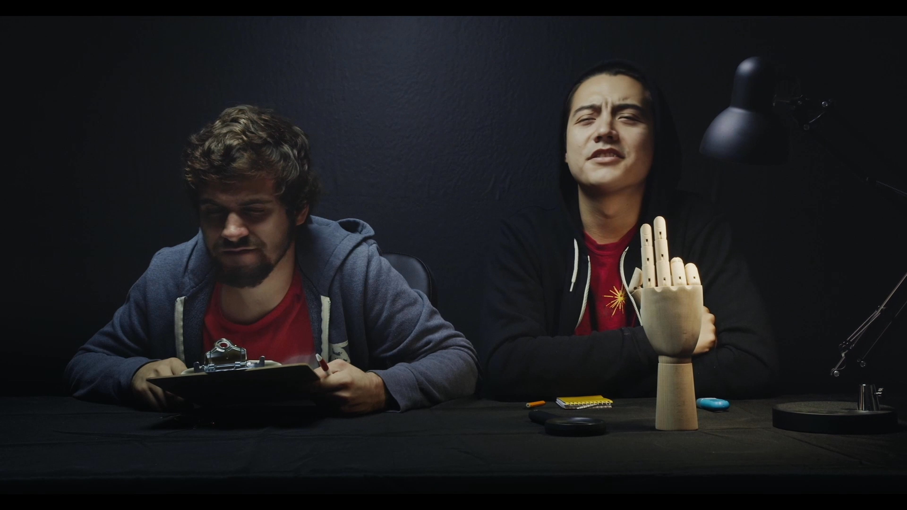 Participants engage in a structured discussion and creative exchange while seated at a desk featuring a mannequin hand prop in a dimly lit studio.