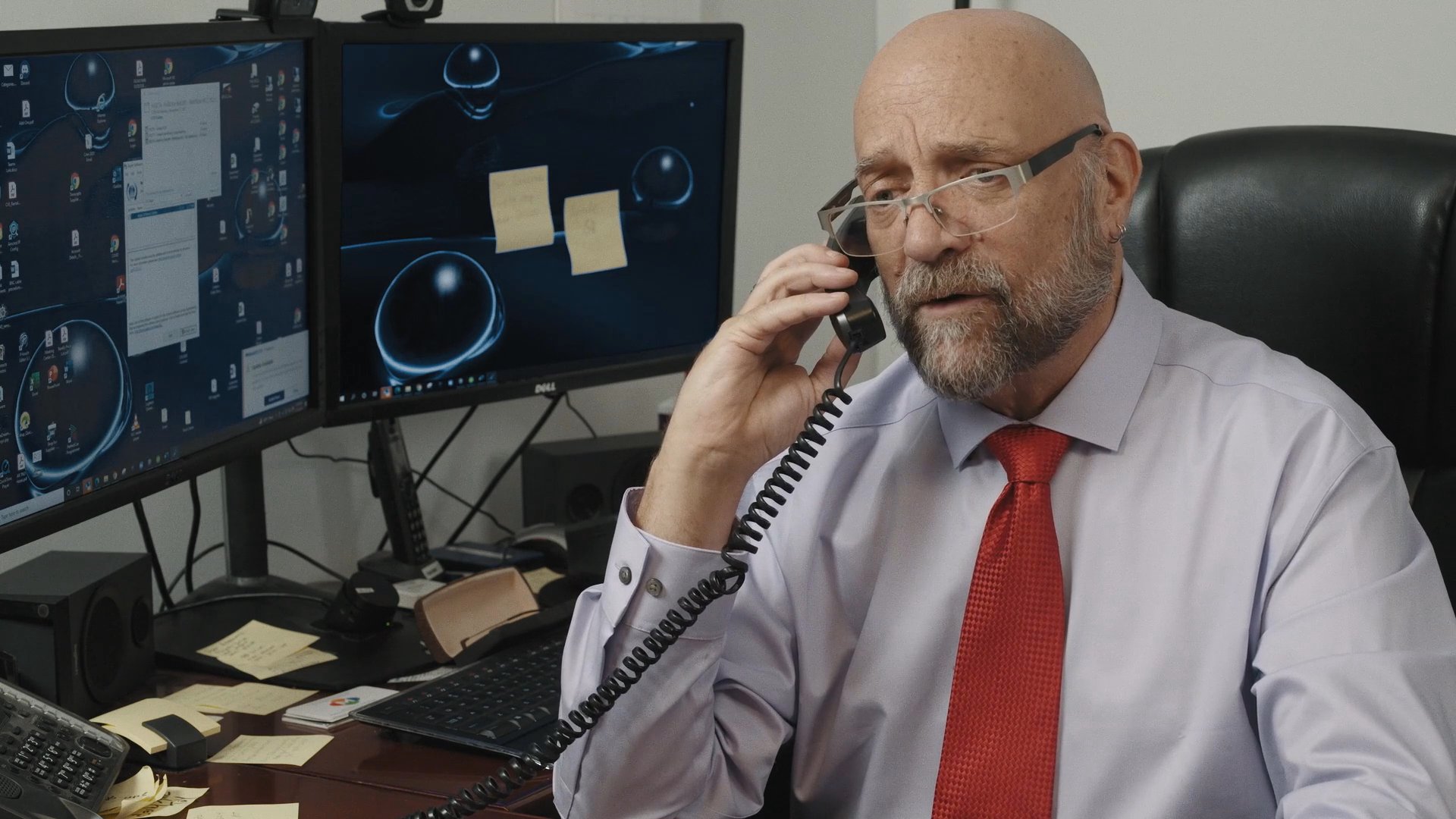 Two individuals engage in separate, serious phone conversations from their respective locations. The scene highlights the nature of professional communication and remote collaboration in a corporate setting.