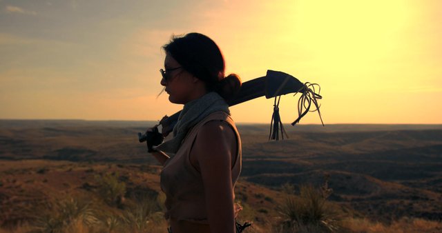 A woman walks on the edge of a hill with a weapon 