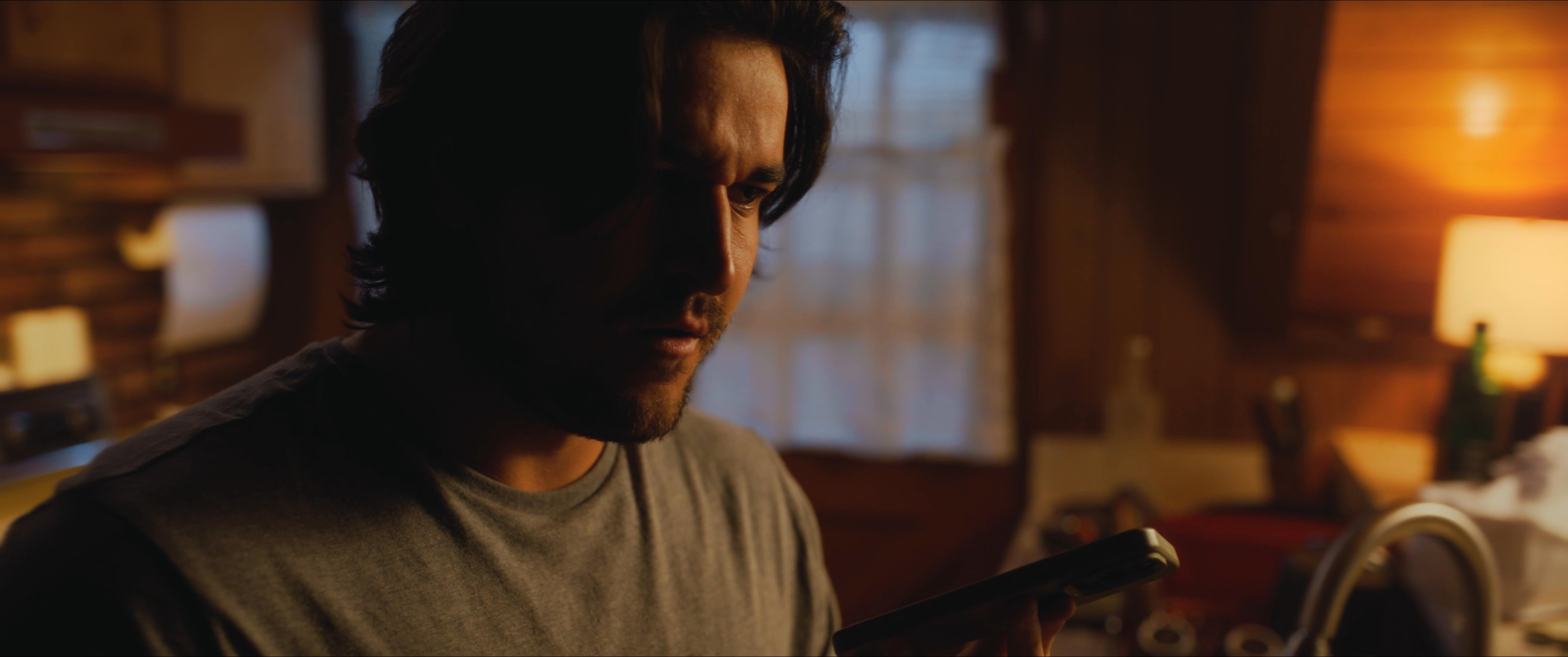 A man engages in a focused telephone conversation within a dimly lit, warm-toned residential interior. The environment suggests an evening setting as he communicates while standing near a kitchen counter.