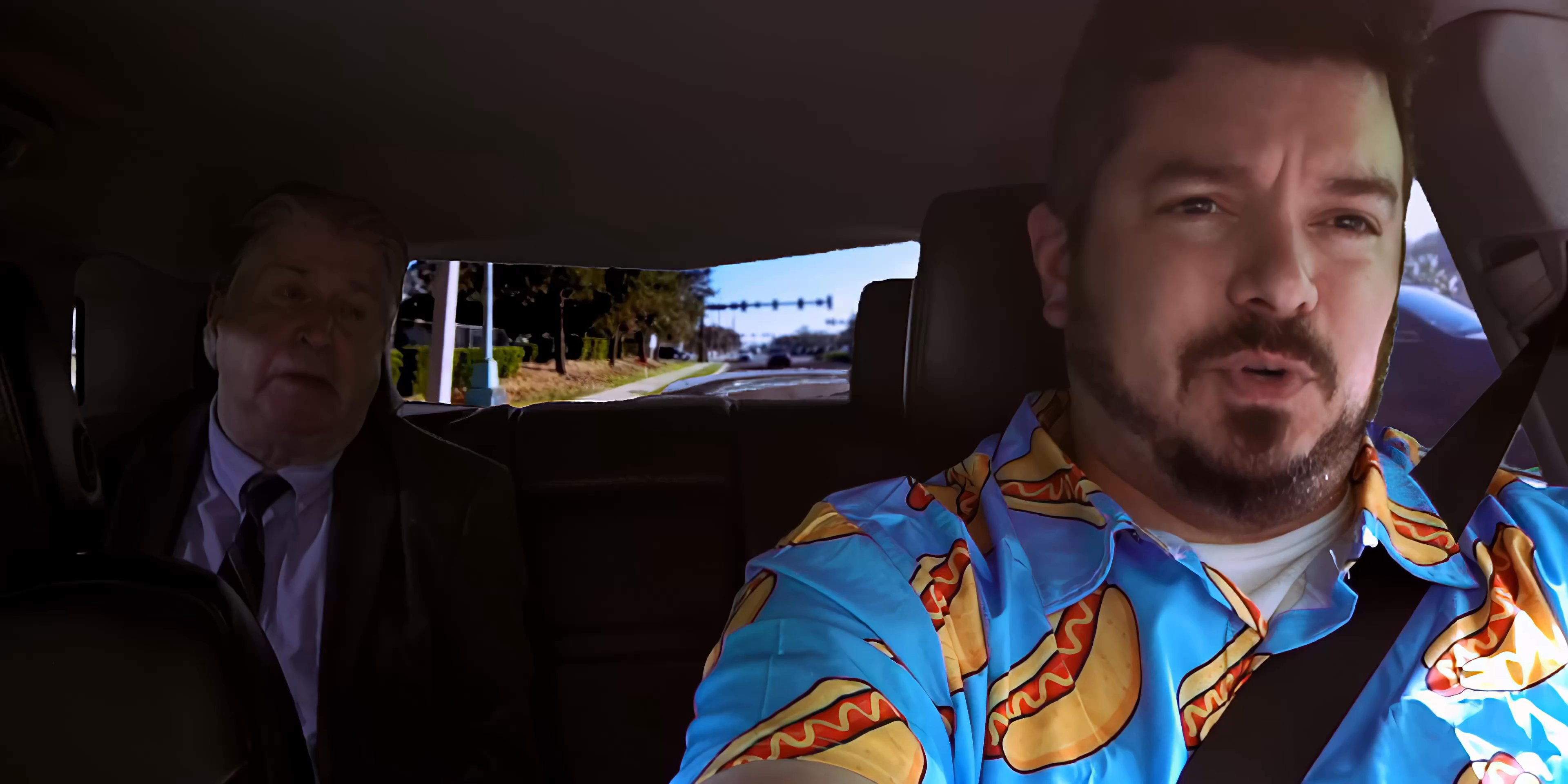 Two individuals engage in a professional discussion while traveling as passenger and driver in a vehicle through an urban environment.