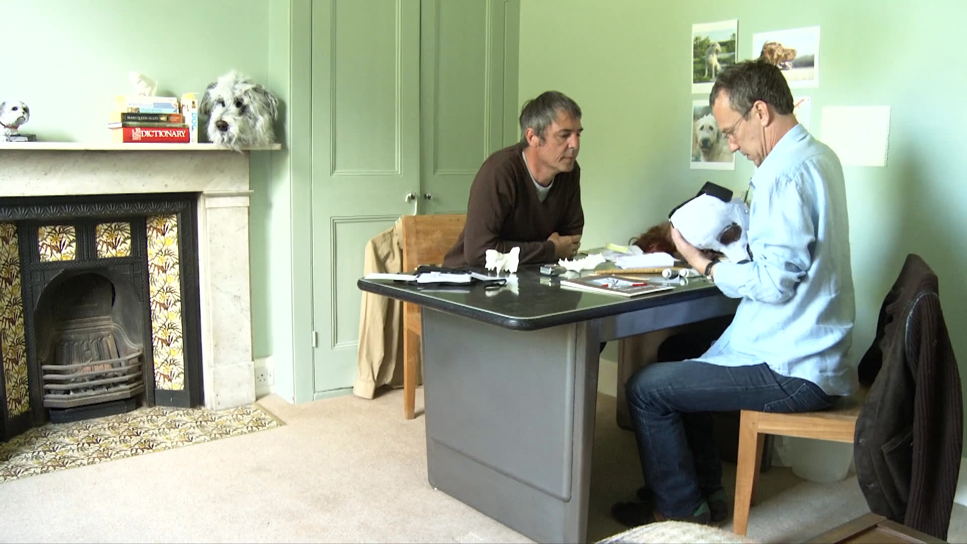 An artisan works with a collaborator to refine and adjust the fit of a handcrafted animal-themed mask in a studio setting. The session concludes as the creator transitions to a computer workstation to document the process.