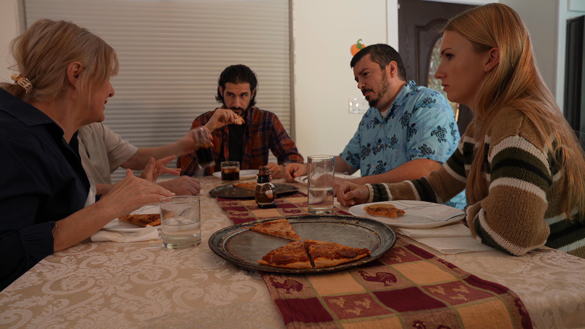 A group of adults engages in conversation while sharing a meal at a table decorated for the Thanksgiving holiday. The participants gesture and interact while eating, highlighting a communal festive atmosphere.