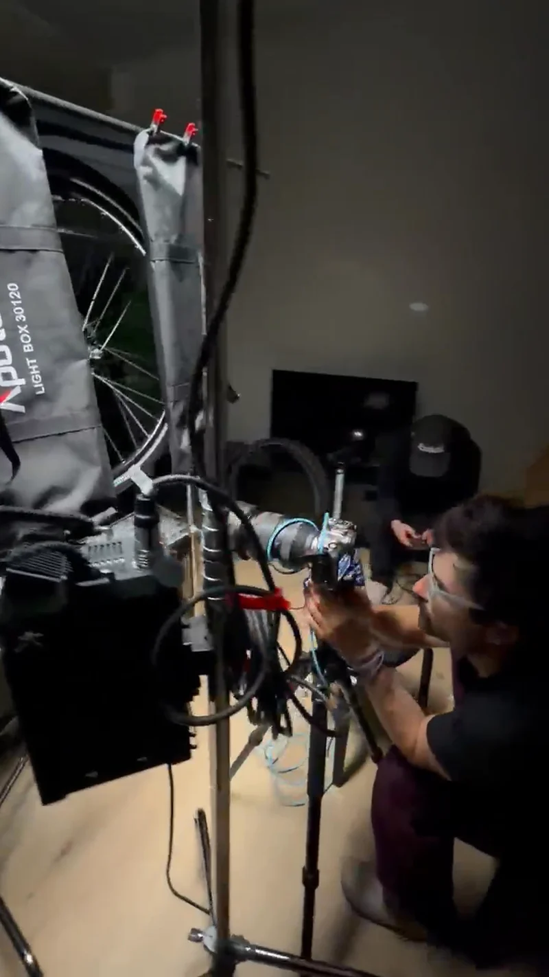 A crew member adjusts a camera amid lighting equipment and cables on an indoor production set.