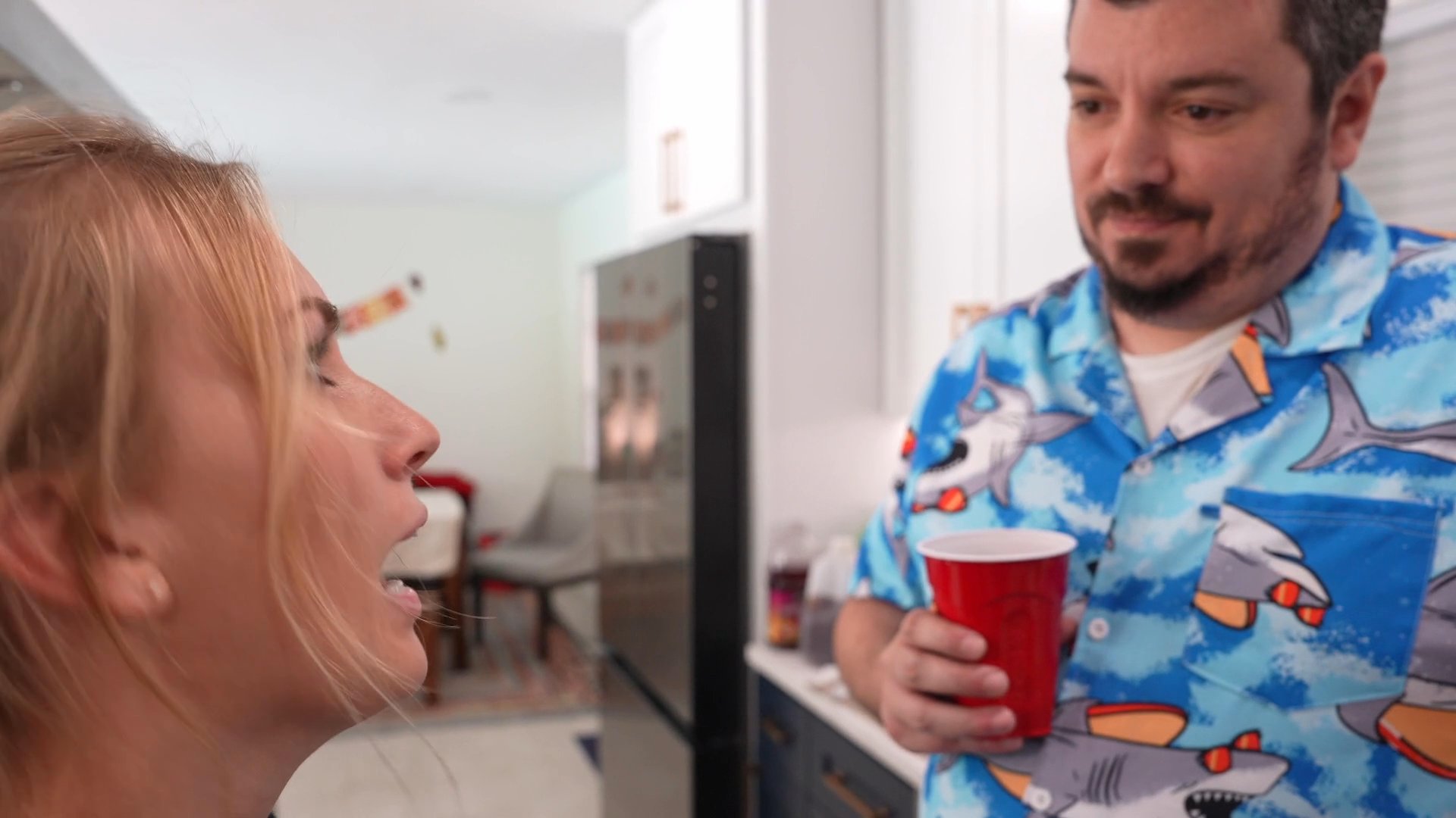 A woman expresses intense frustration and complains to a man in a kitchen setting while he listens while holding a red plastic cup.