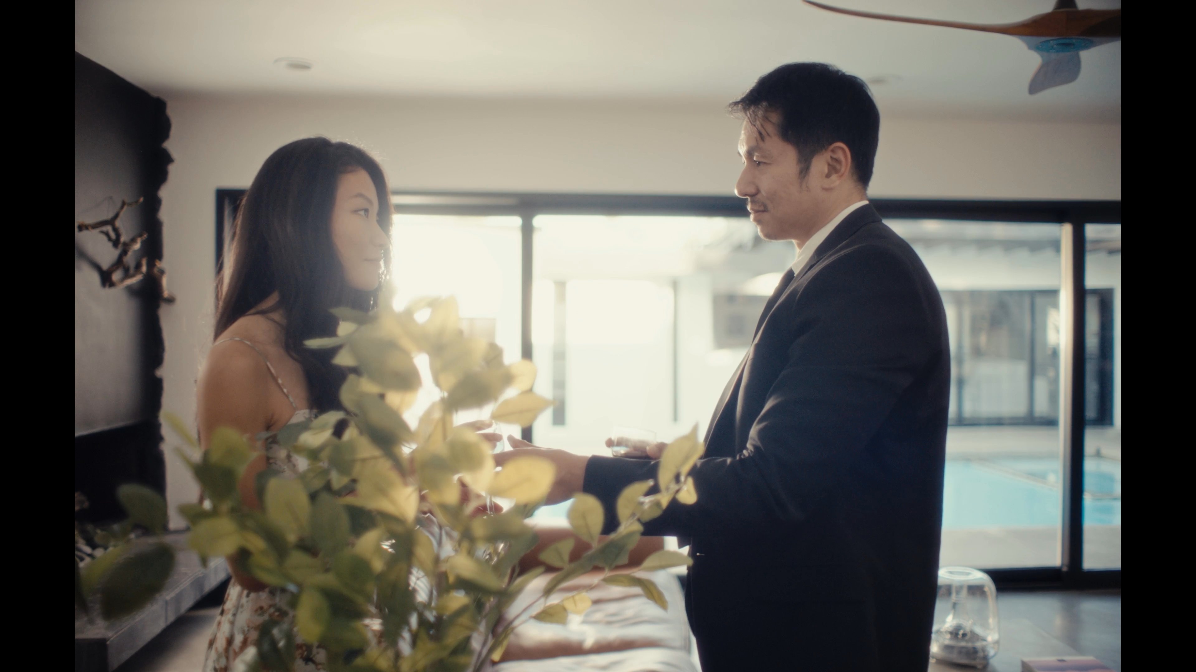 A man in a suit surprises a woman with a marriage proposal in a sunlit living room. They share an intimate and joyful moment together.