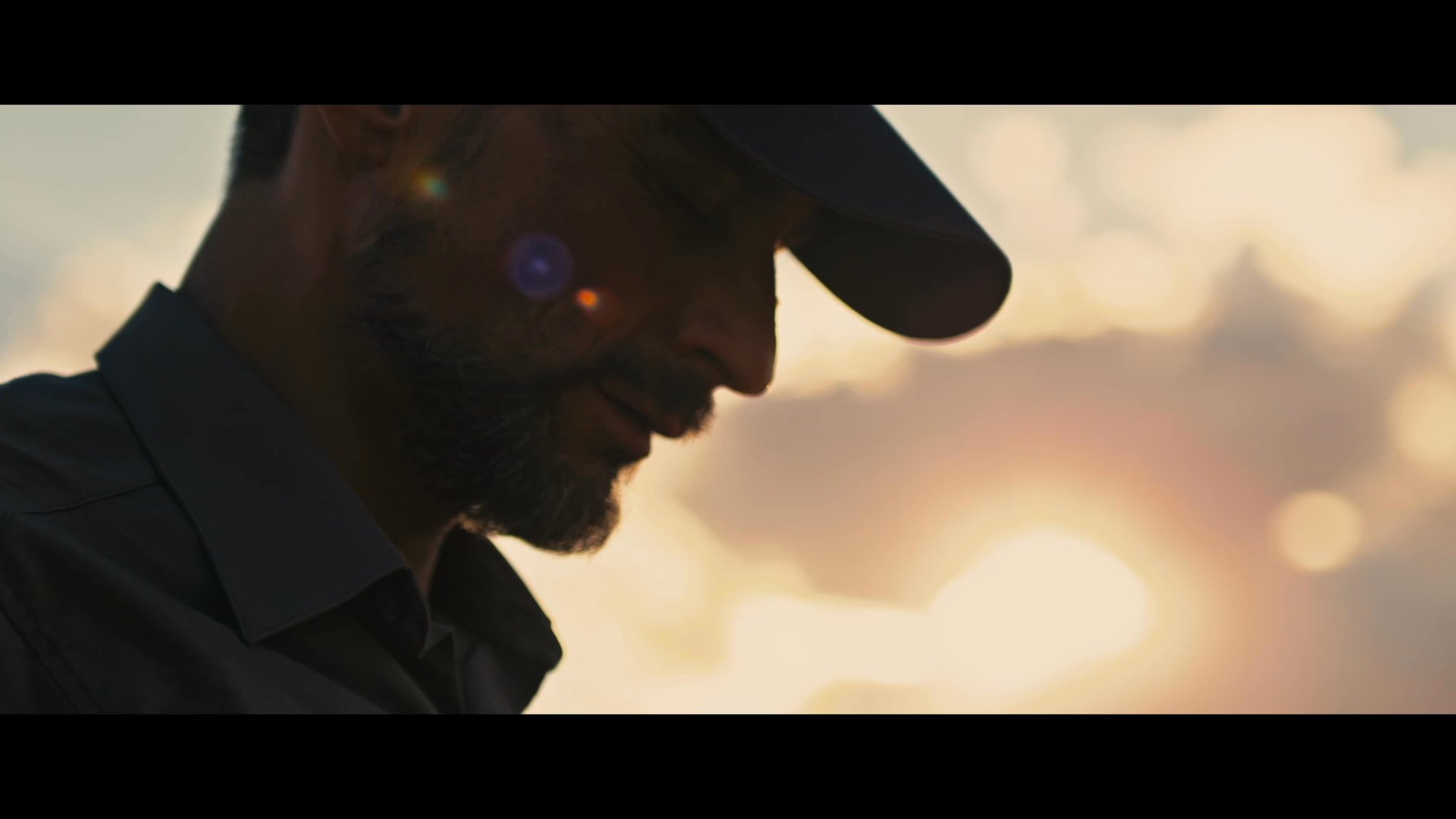 A man walks alone through a vast, sun-drenched desert landscape, eventually pausing to examine a small, unique object he has found.