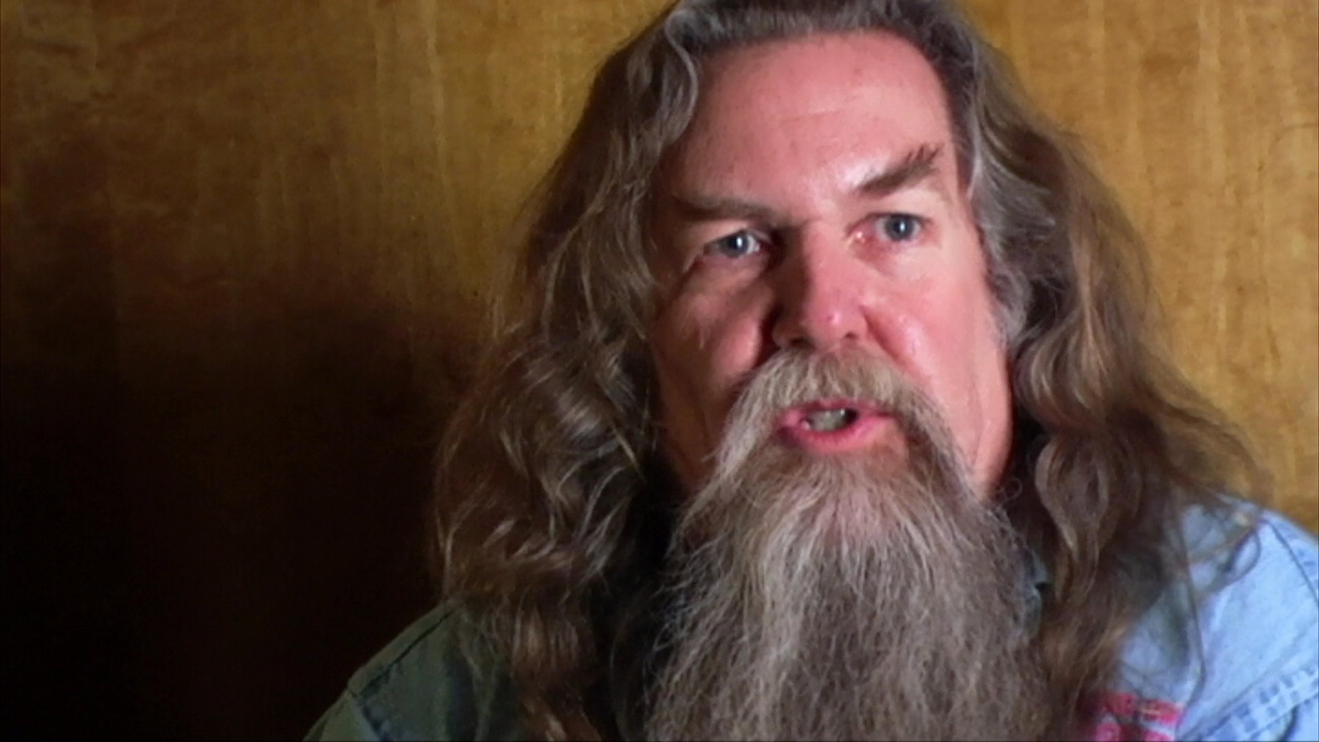 A man with a long beard speaks expressively while gesturing, likely sharing a personal story or delivering an educational narrative.
