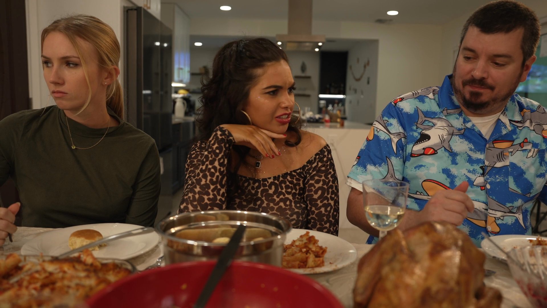 A group of people enjoys a holiday meal together around a dining table decorated with seasonal banners. The individuals engage in conversation while sharing food in a residential setting.