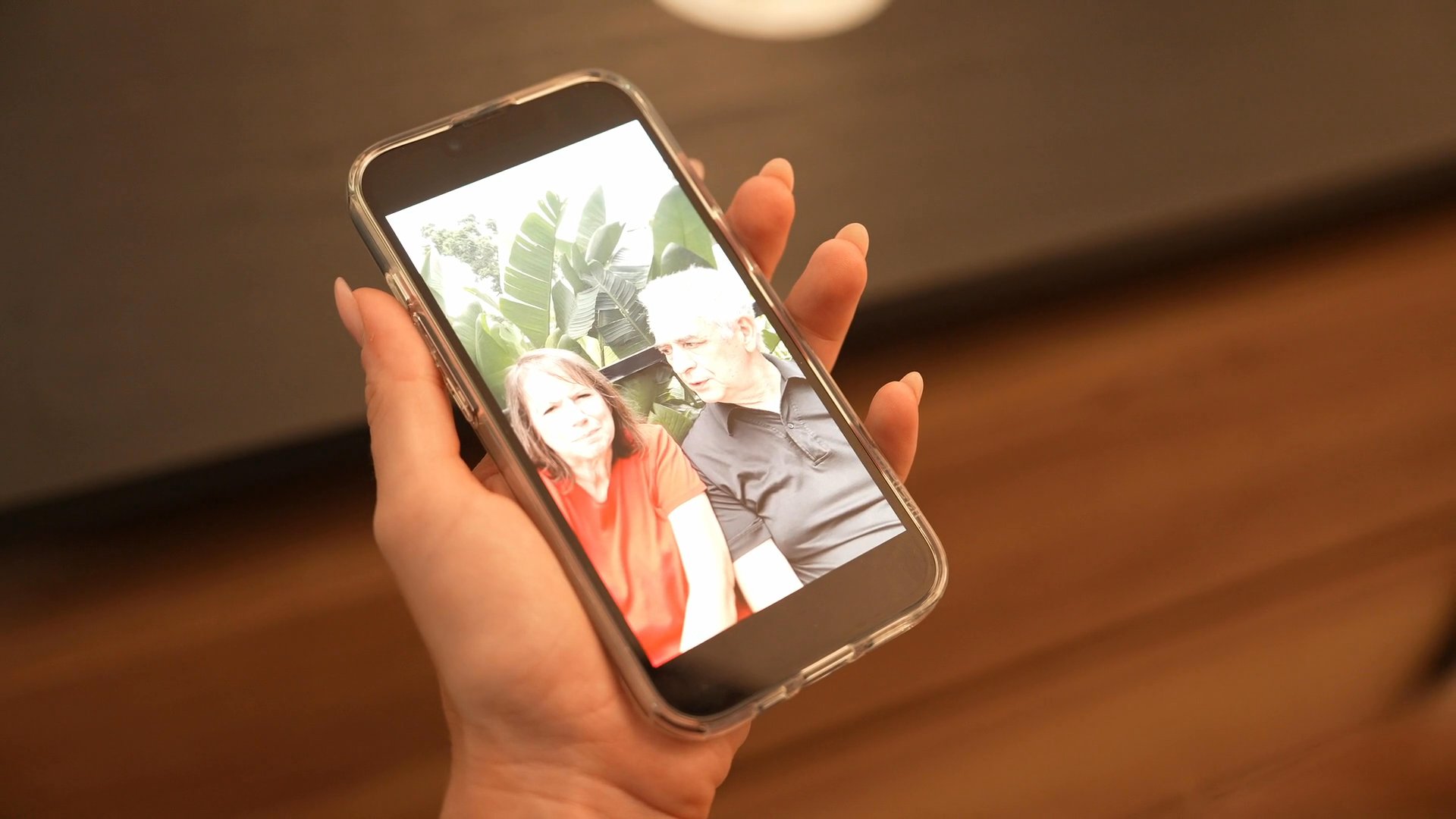 A person views a video call on a smartphone screen while standing in front of a mirror, showing both their real-world reflection and the digital interaction.