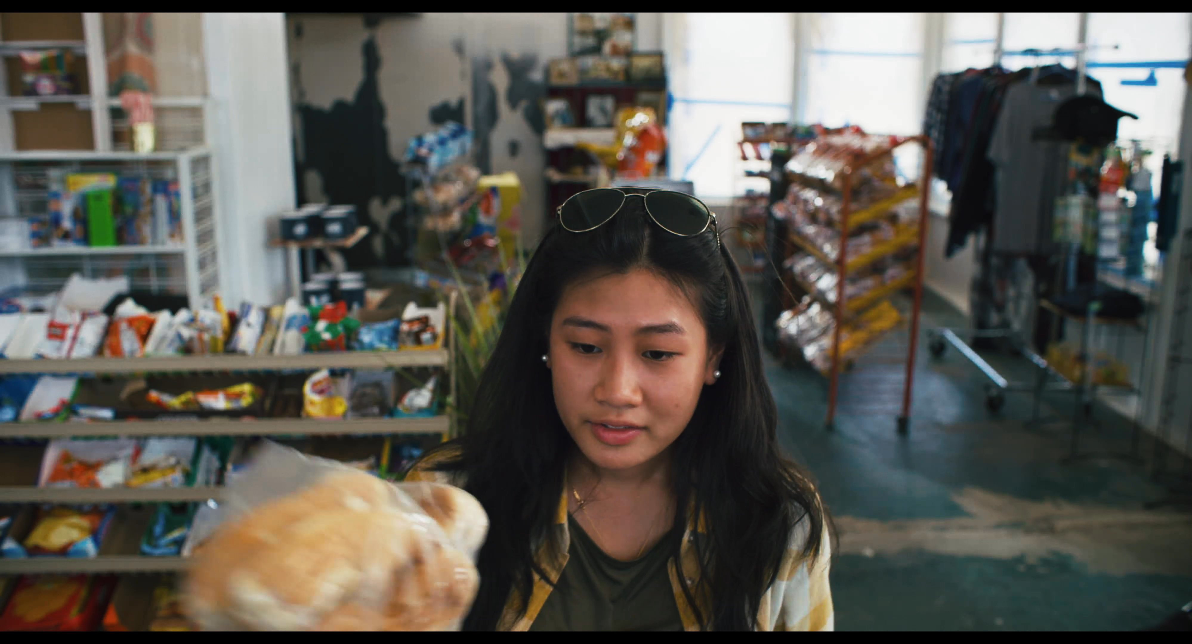 A customer interacts with a store clerk at the checkout counter while another person walks through the retail aisles in the background.