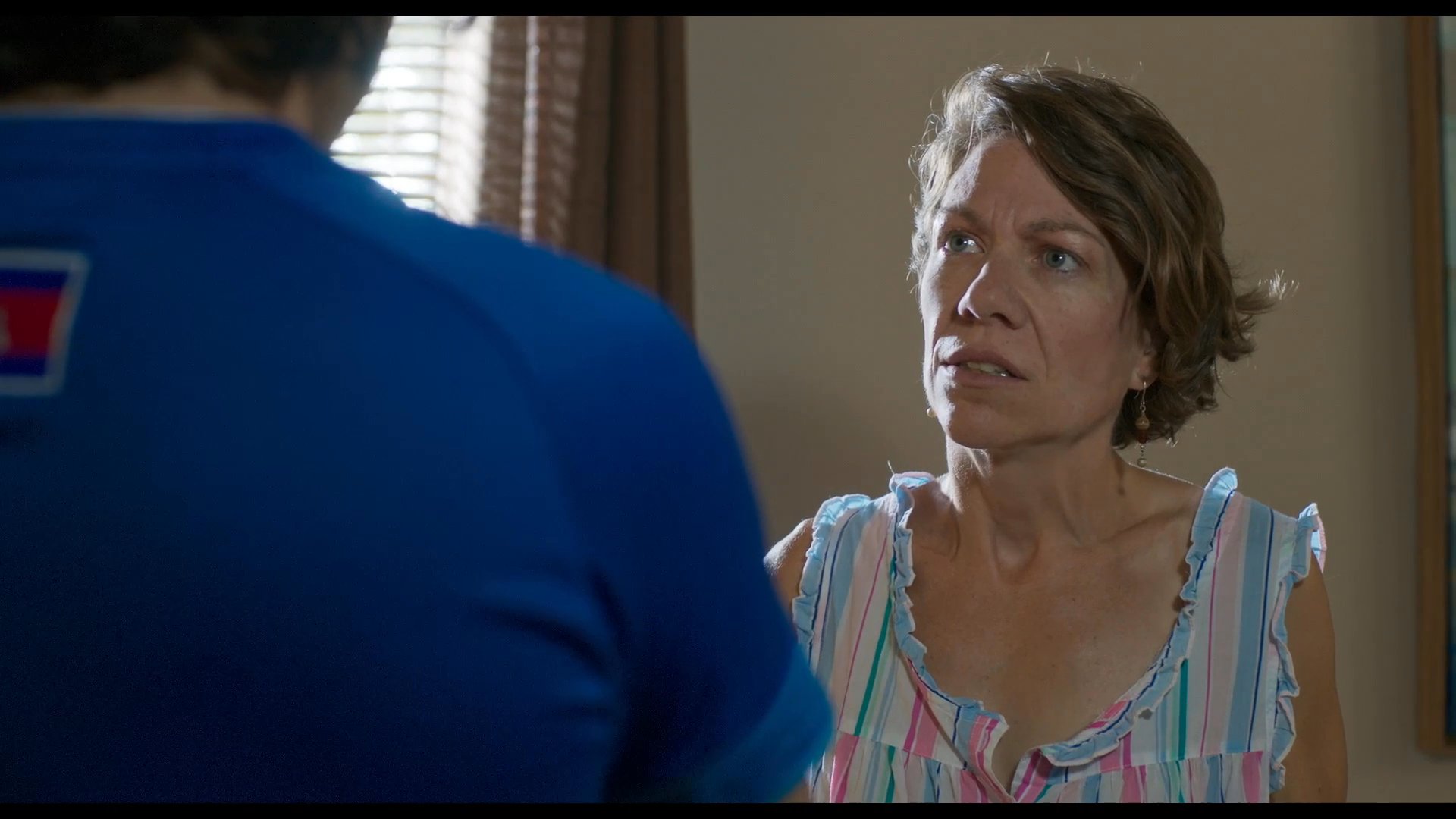A young man wearing a blue sports jersey engages in a serious, emotionally charged conversation with an older woman inside a home. The pair exchange expressive glances while navigating a difficult discussion.