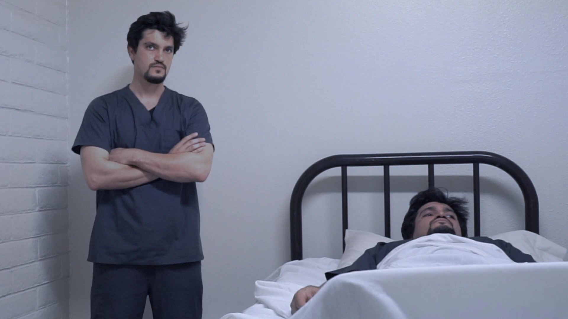 A medical caregiver stands by a bedside, observing a patient resting in a hospital setting while an older woman arrives to visit. The scene highlights the clinical environment and the routine of patient care.
