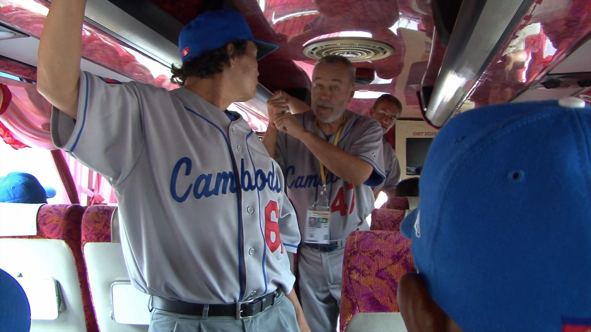 A spiritual advisor addresses the Cambodian baseball team while riding on a bus. He speaks to the players, emphasizing team unity and preparation.