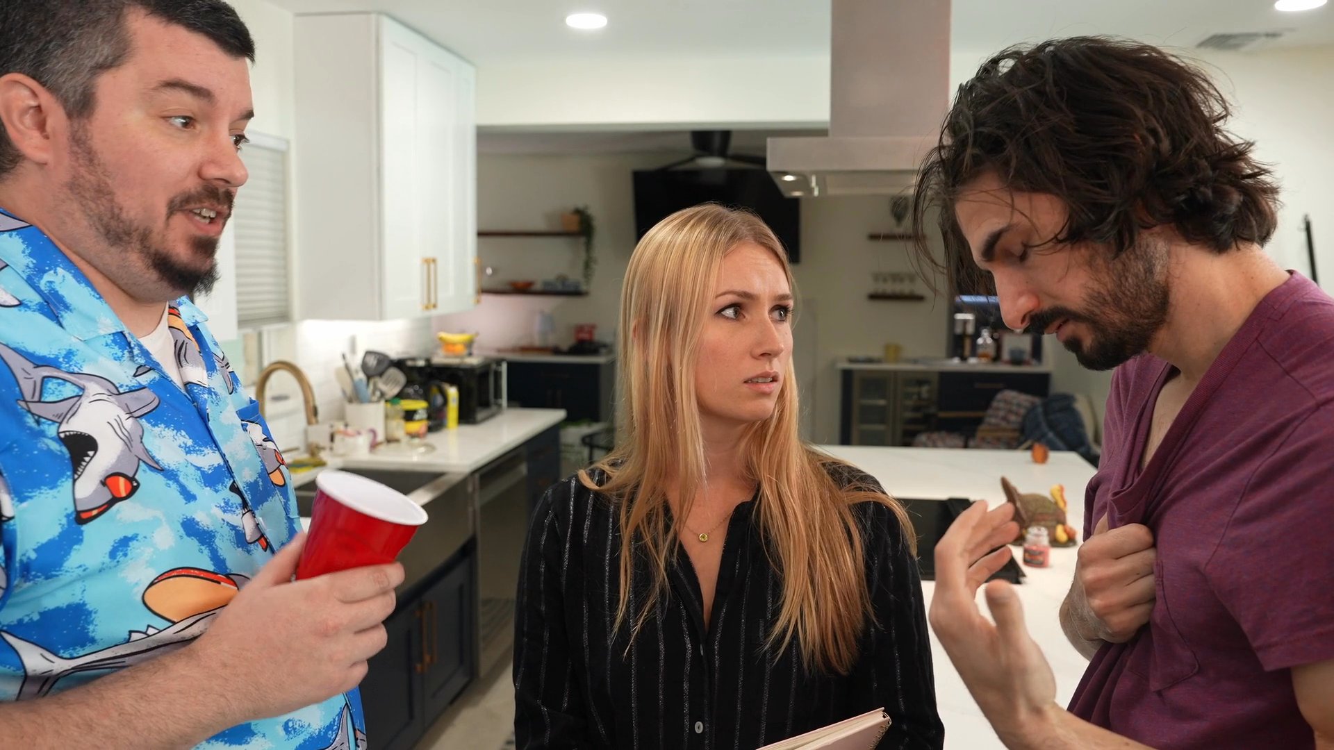 Two distinct groups of people engage in separate, animated conversations within a home kitchen setting. The individuals exchange dialogue while standing in kitchen spaces decorated with seasonal banners.