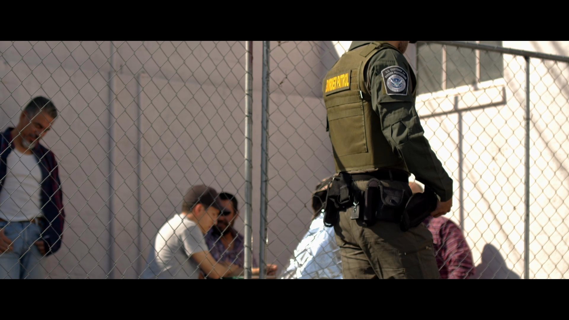 A group of migrants is apprehended in a desert environment and processed by border patrol agents at a secure facility. The scene illustrates the logistical coordination of immigration enforcement and detention operations.