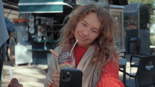 A girl smiling and taking a selfie at a street café