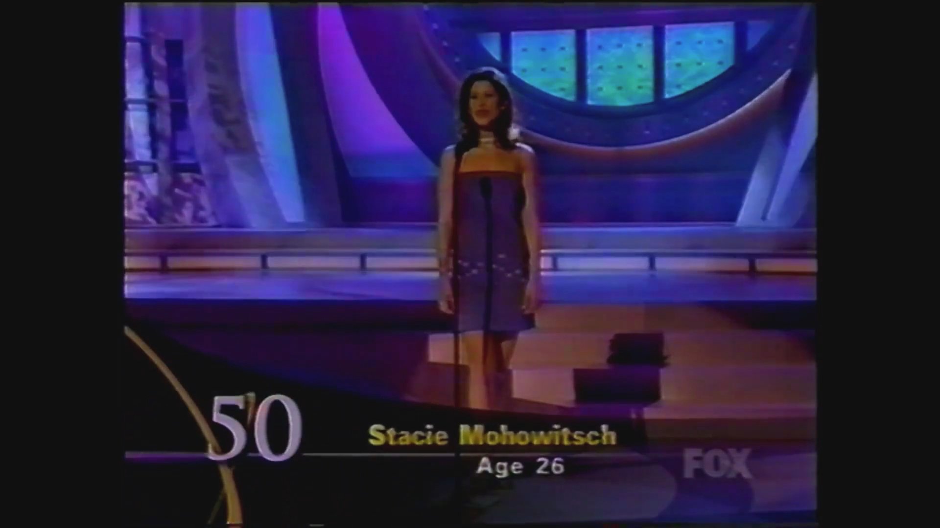 Contestants are introduced sequentially on a formal television stage, followed by commentary from the pageant hosts.