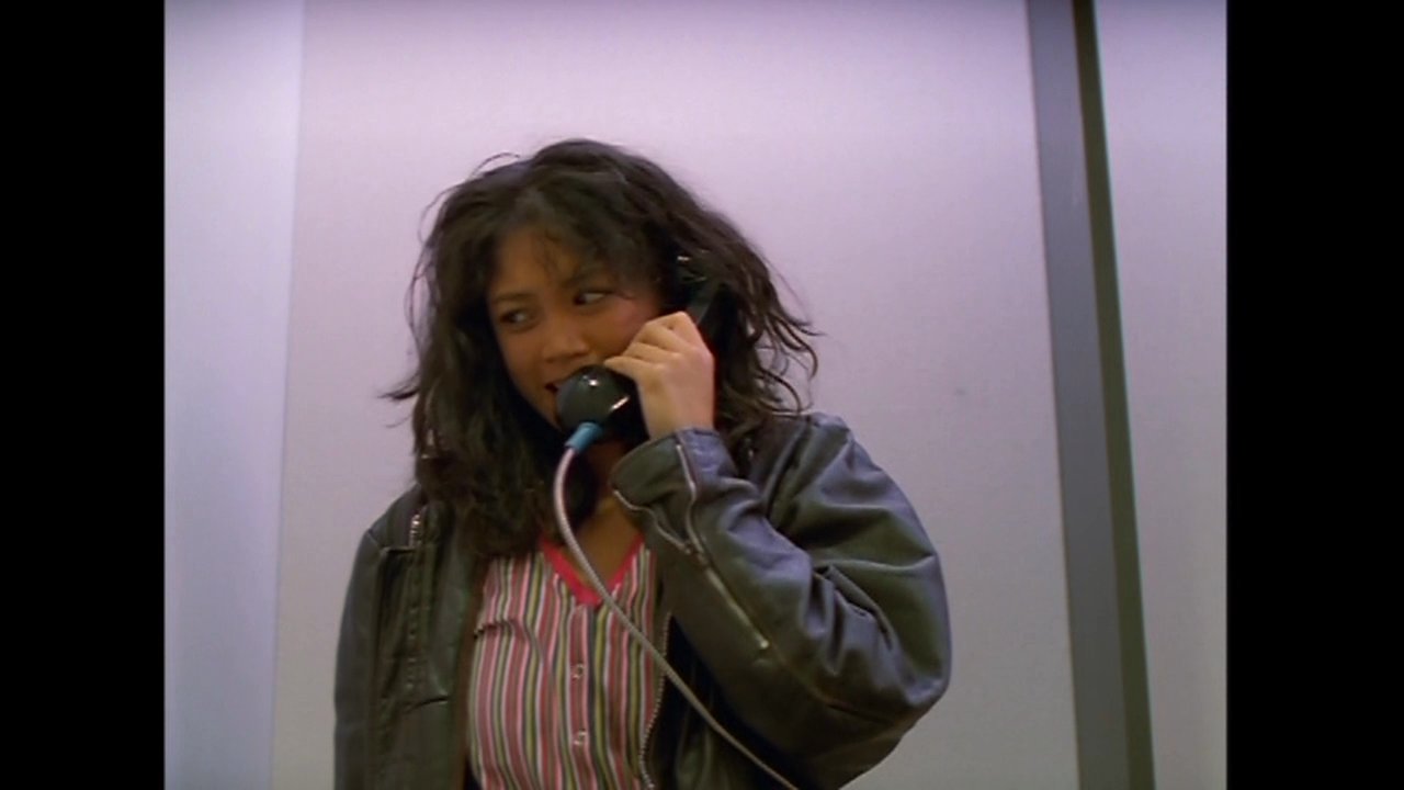 A man awakes in bed to answer a telephone call, while a woman simultaneously speaks on a separate line. The scene transitions to the man checking a door peephole before engaging in a face-to-face interaction.