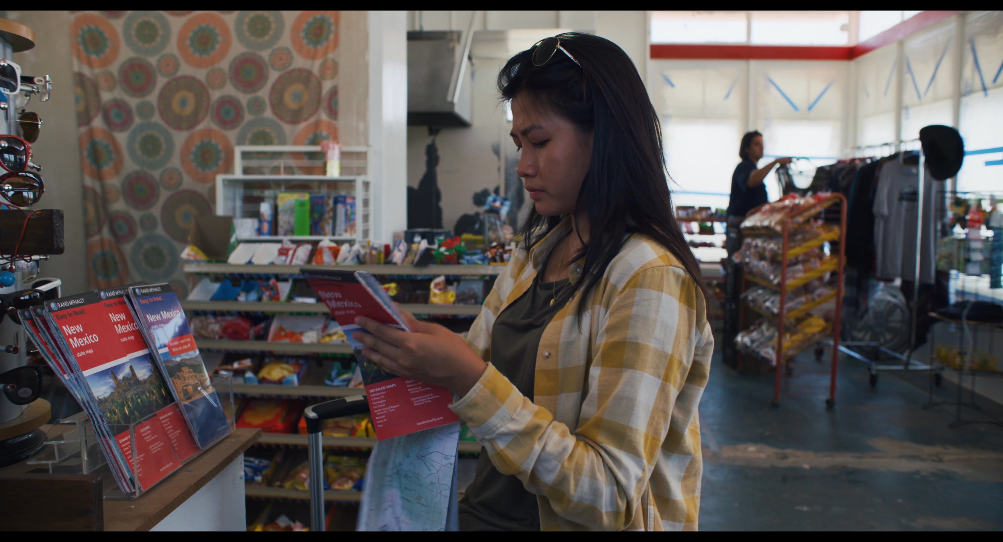 A woman stands in a retail shop and evaluates a printed travel map while planning her upcoming journey.