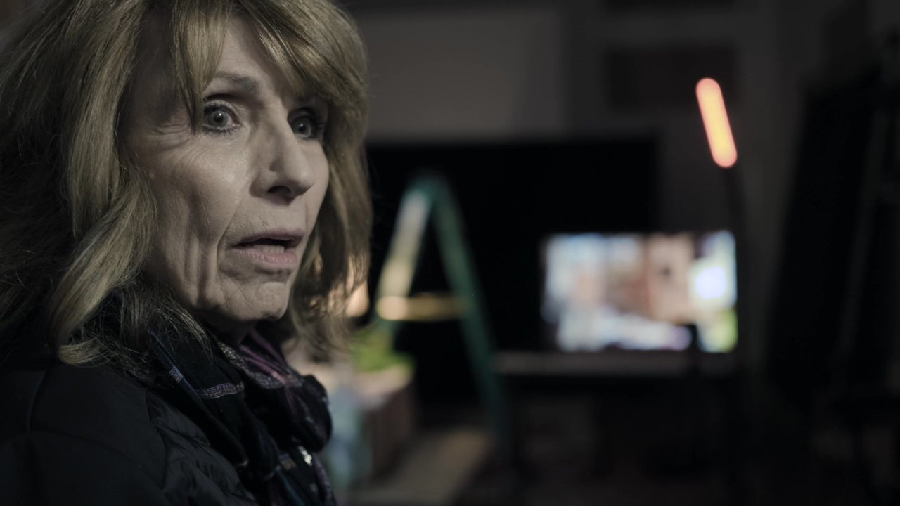 A woman engages in an intense, private conversation in a dimly lit studio environment before entering a film production set. The scene transitions to reveal the professional workspace and technical equipment involved in the filming process.