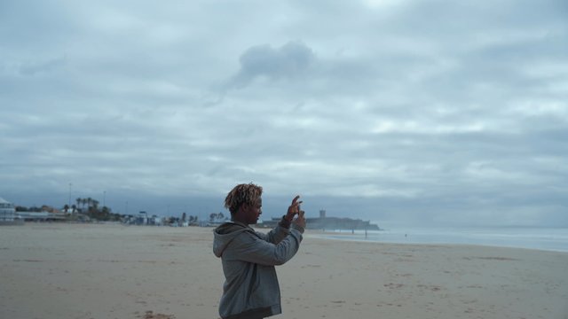 A guy standing on the sandy beach and photographing the sea