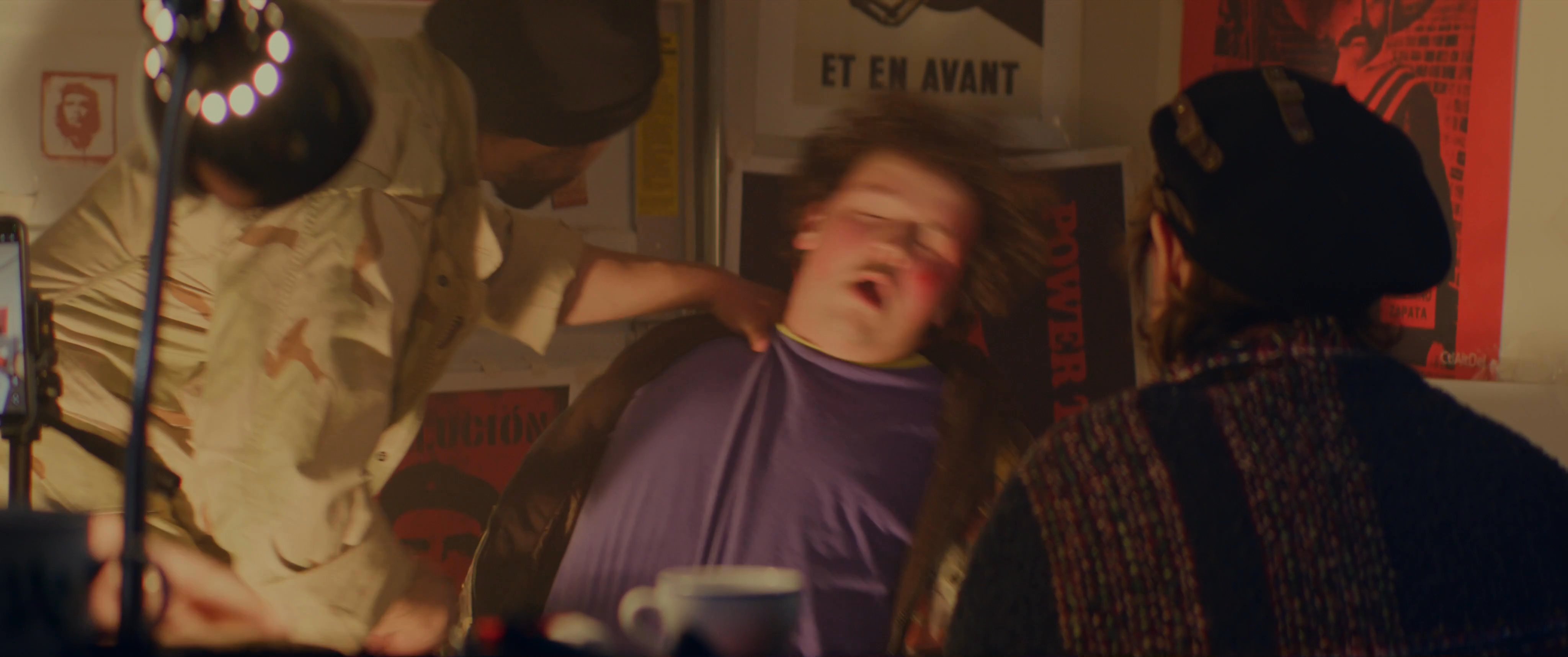 An intense encounter unfolds as a man is held captive and subjected to questioning by armed individuals in a dimly lit, industrial setting. The scene highlights mounting psychological pressure and conflict between the individuals involved.