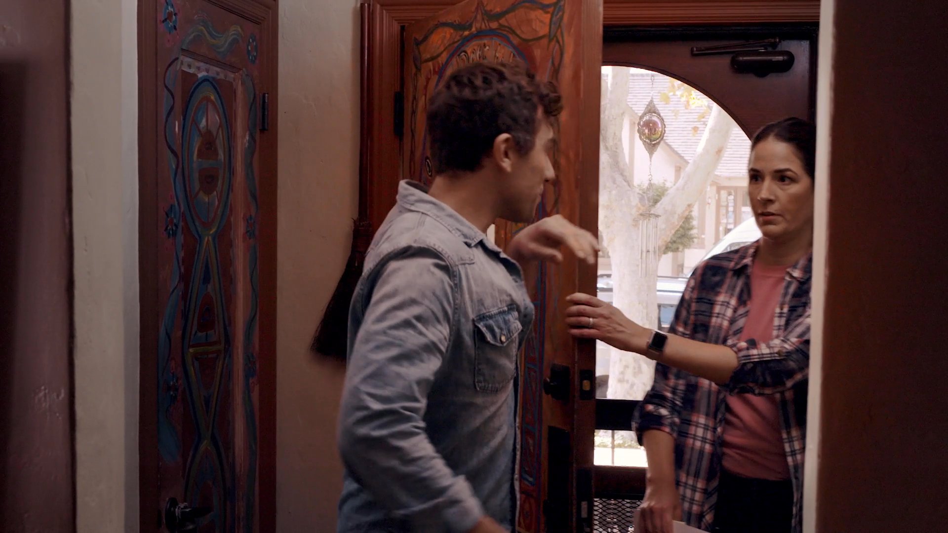 A man arrives home and enters a residence, greeting a woman waiting by the decorated doorway. The scene transitions from opening production credits to a brief interpersonal exchange.