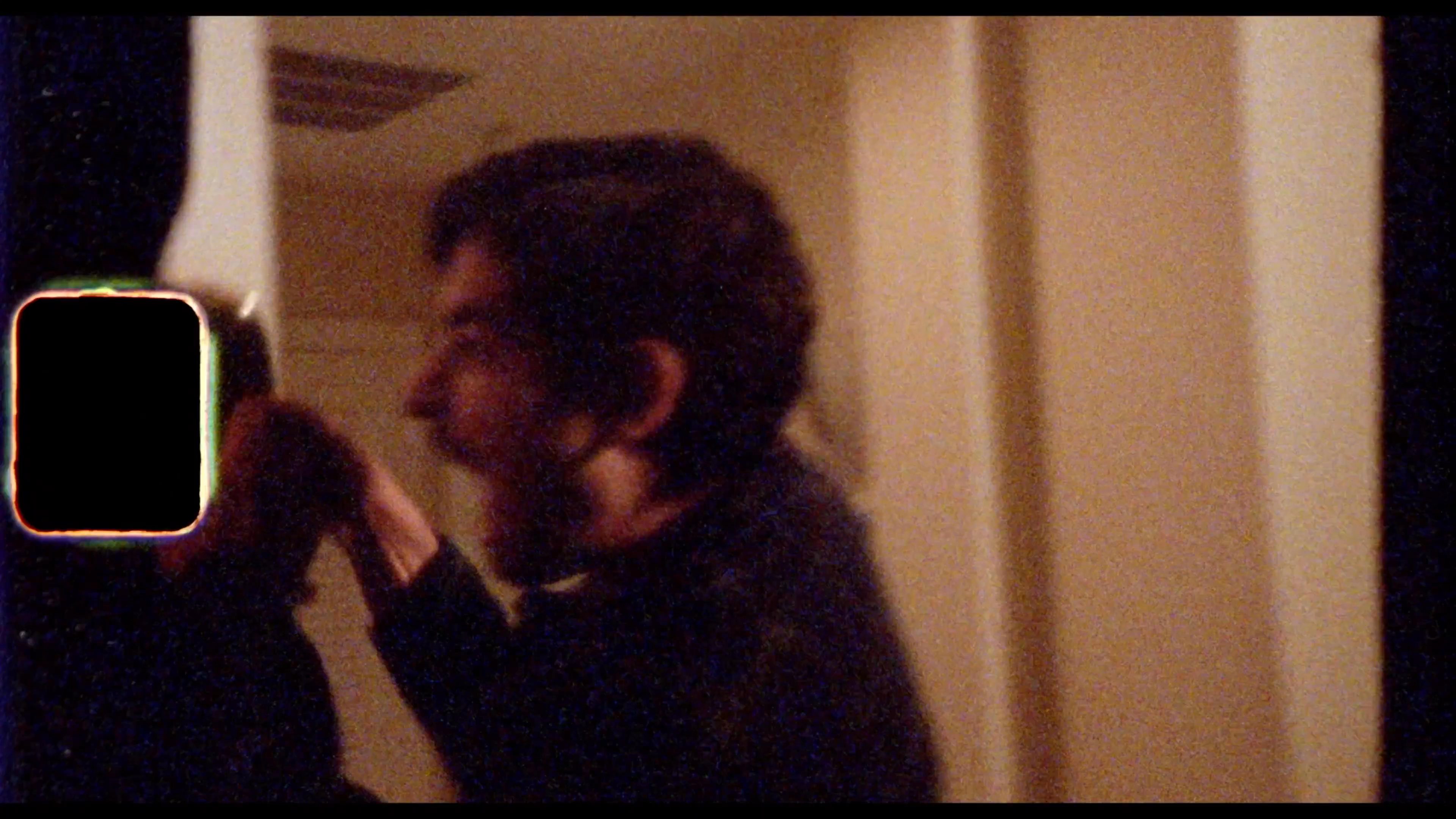 Two individuals engage in a conversation at a video rental store while periodically transitioning to film-style footage of movie-related activities. The exchange highlights the interpersonal dynamics between store patrons and staff amidst shelves of physical media.
