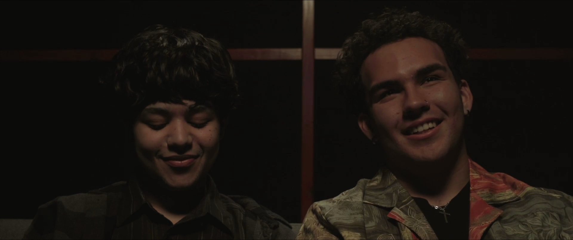 Two individuals share an intimate, dialogue-driven moment outdoors, transitioning to another pair bonding closely in a dimly lit indoor environment.