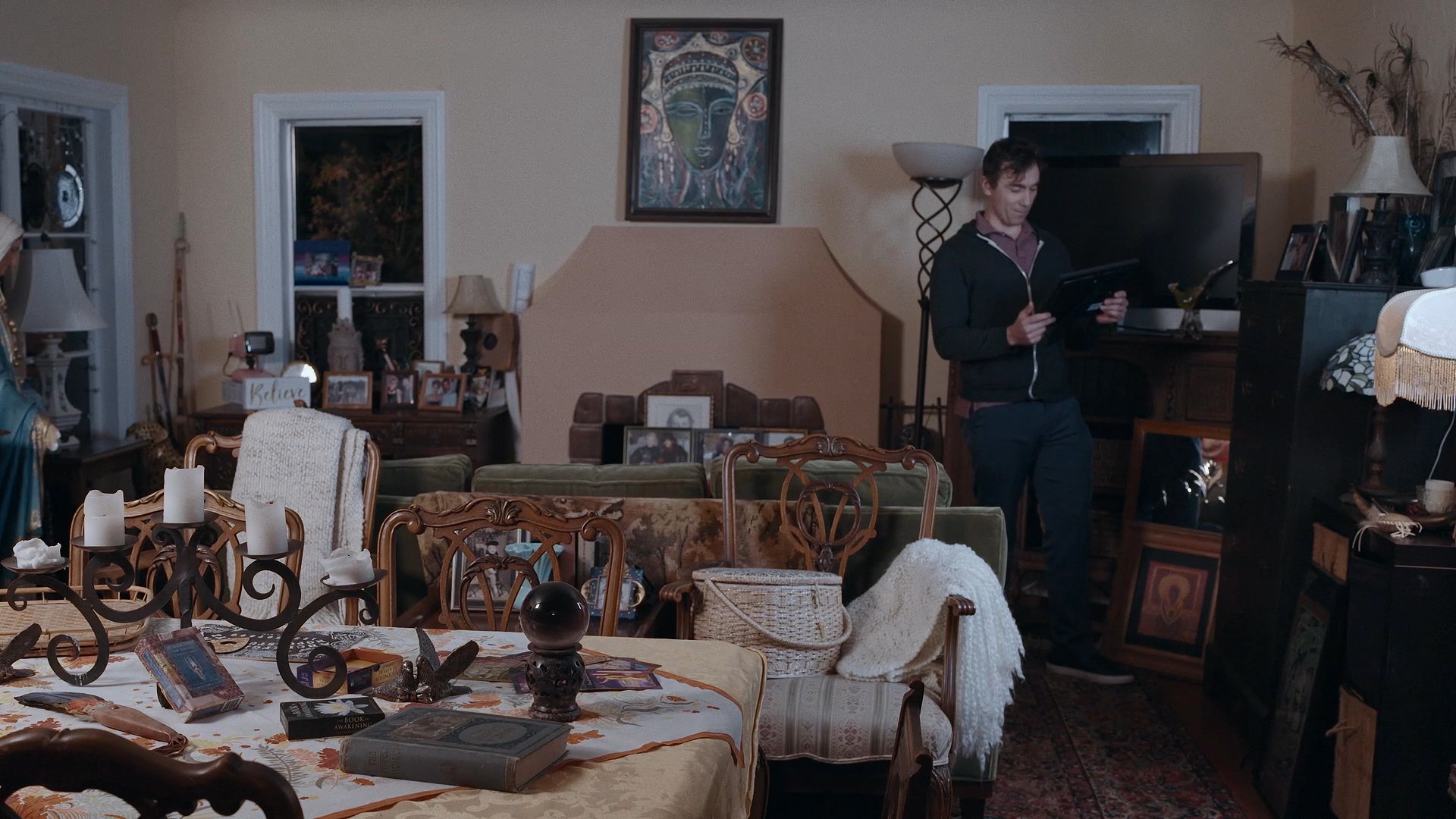 A man navigates a decorated residential living room while holding a tablet to inspect and organize items.