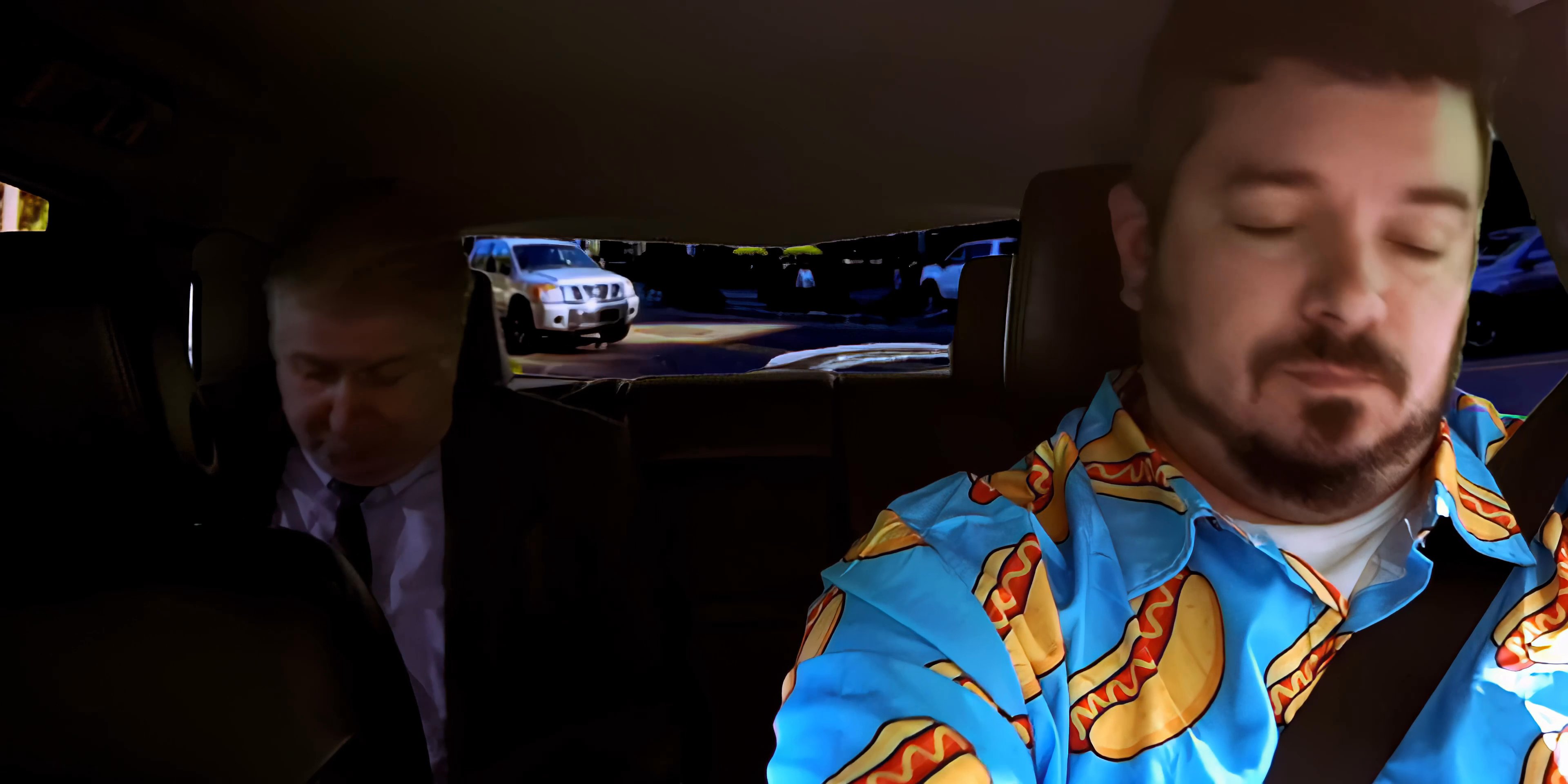 Two men engage in a professional discussion while traveling in a vehicle at night. The driver, wearing a distinct patterned shirt, listens intently as his passenger speaks.